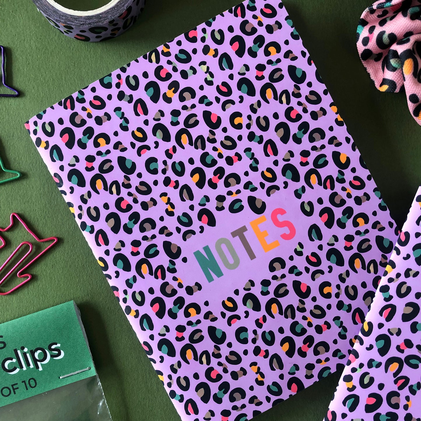 Image shows an A6 notebook in a bright purple with a leopard print pattern featuring pops of neon