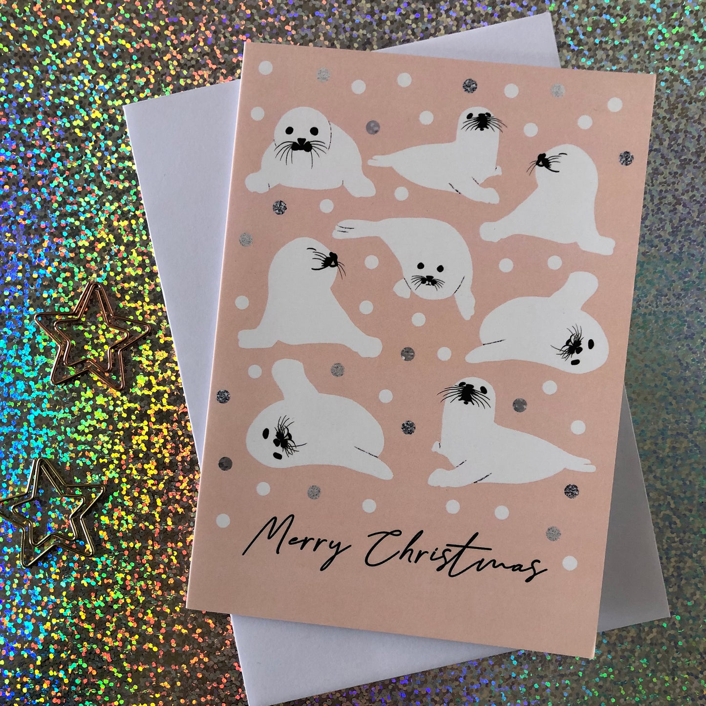 Image shows a peach coloured Christmas card featuring illustrations of baby seal pups.