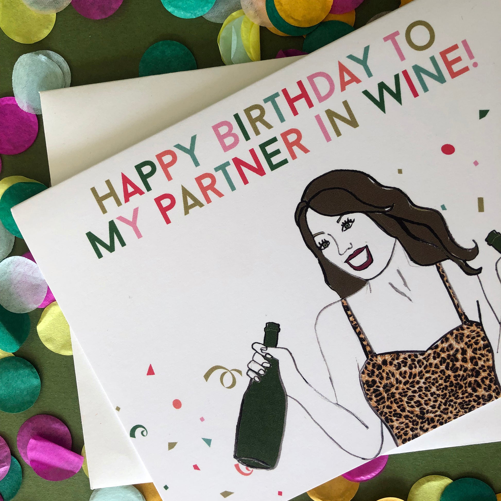 Image shows a fun and fabulous white birthday card with an illustration of a woman in a leopard print top holding 2 bottles of wine and the wording 'Happy Birthday to my partner in wine'..