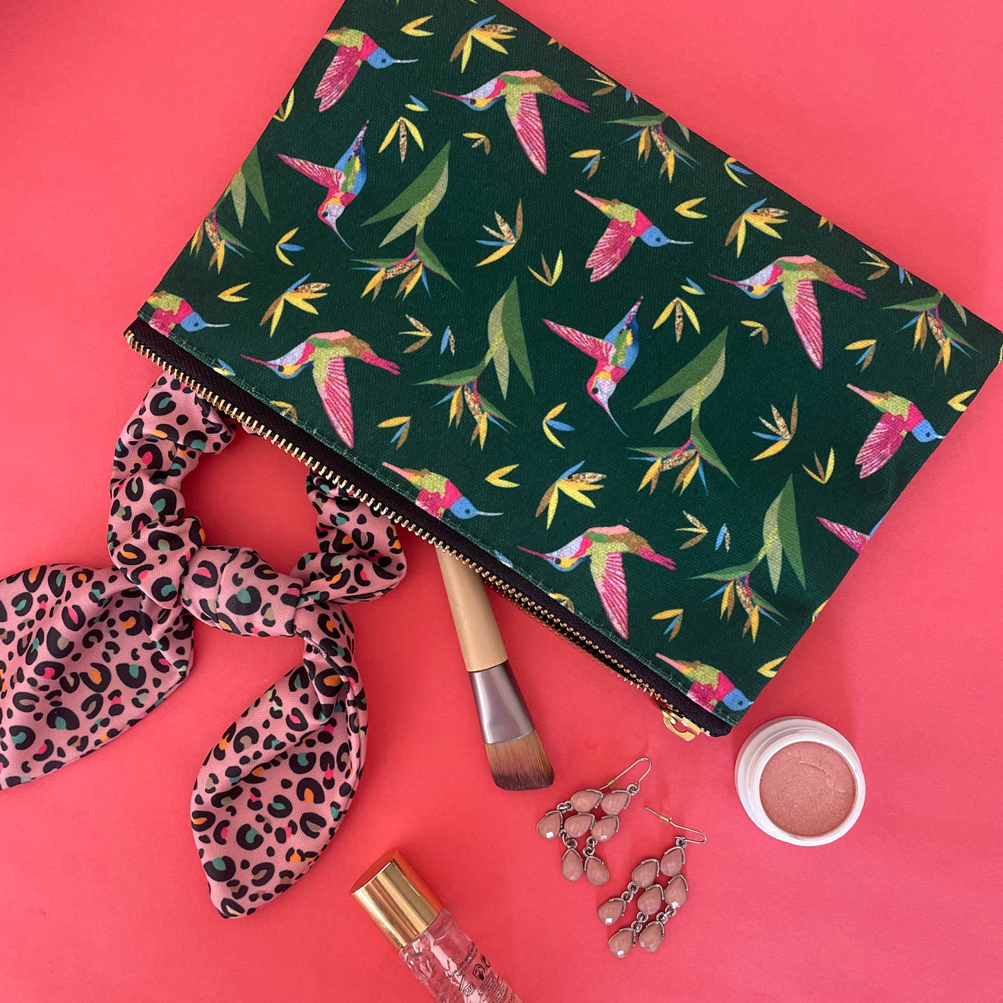Image shows a forest green coloured zip pouch with a colourful hummingbird print on it.