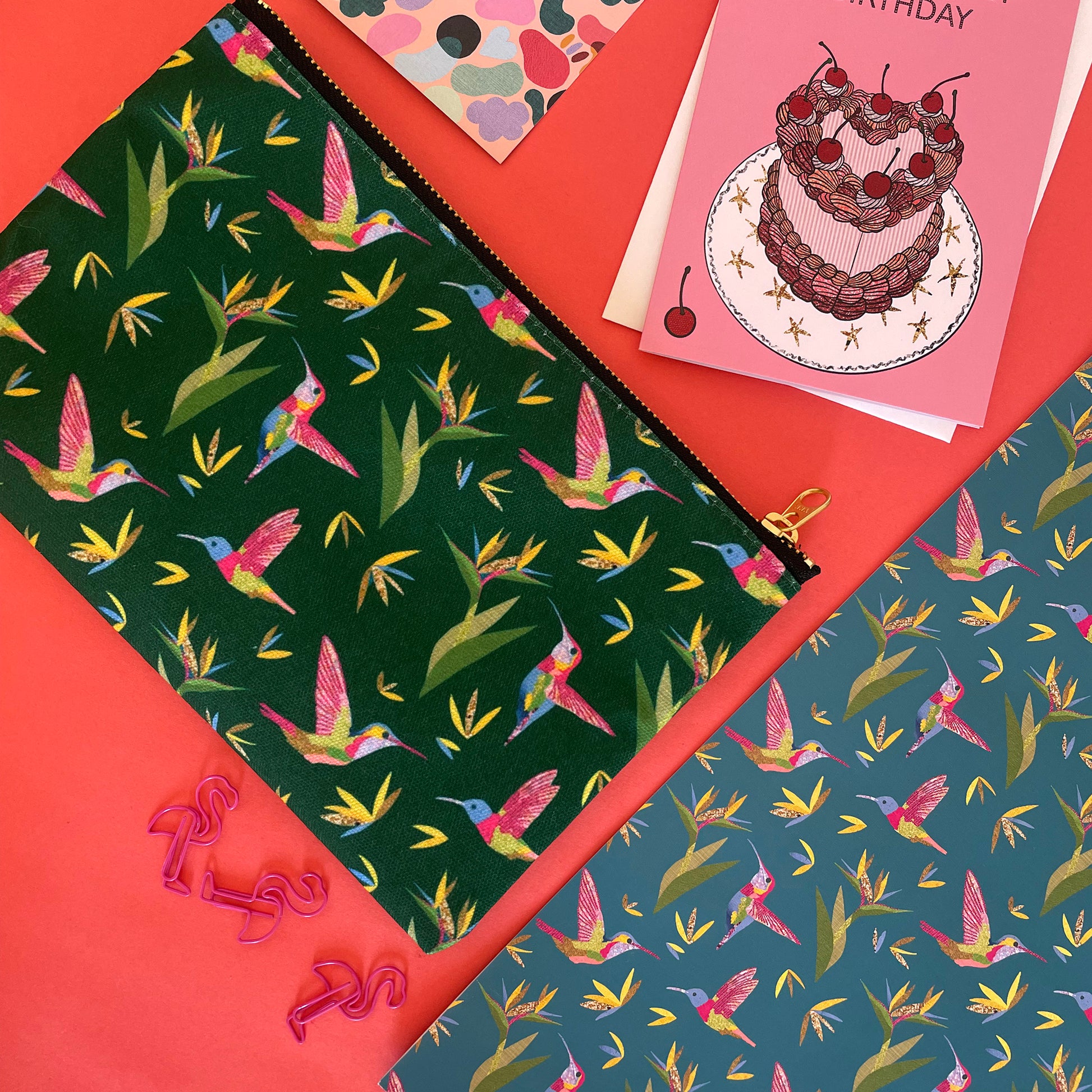 Image shows a forest green coloured zip pouch with a colourful hummingbird print on it.