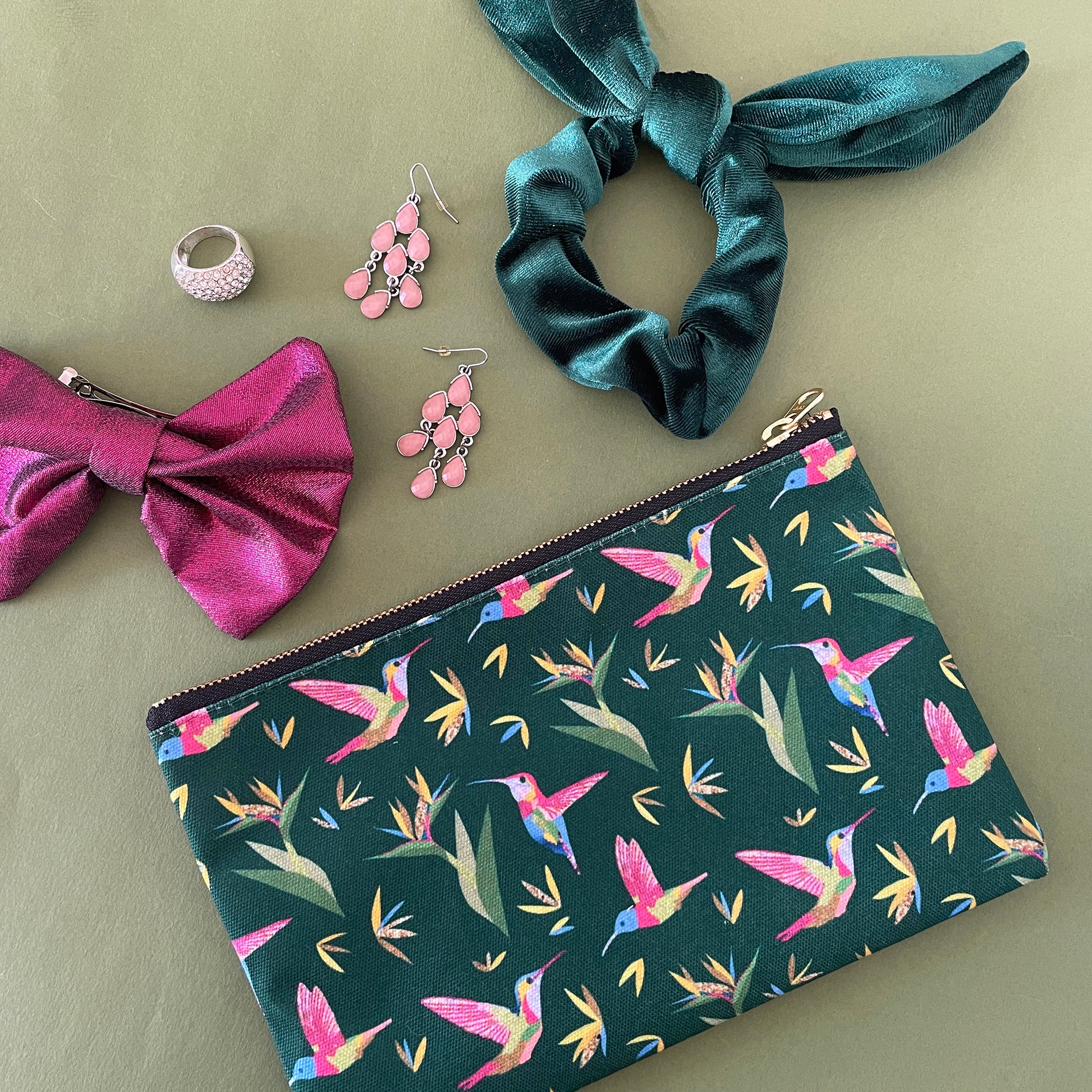 Image shows a forest green coloured zip pouch with a colourful hummingbird print on it.