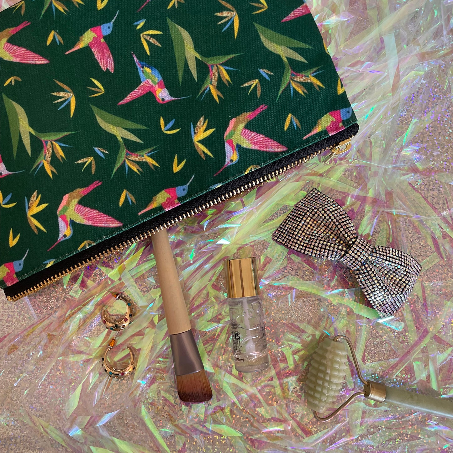 Image shows a forest green coloured zip pouch with a colourful hummingbird print on it.