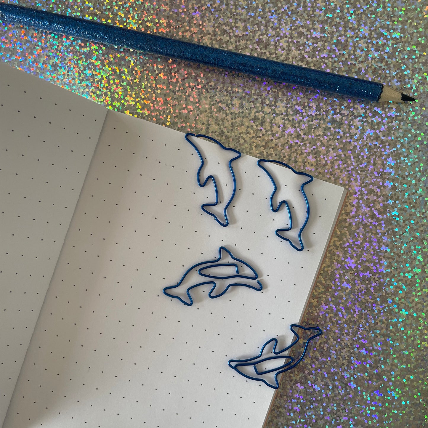 Image shows a fun set of 10 dolphin shaped paper clips in bright, metallic blue