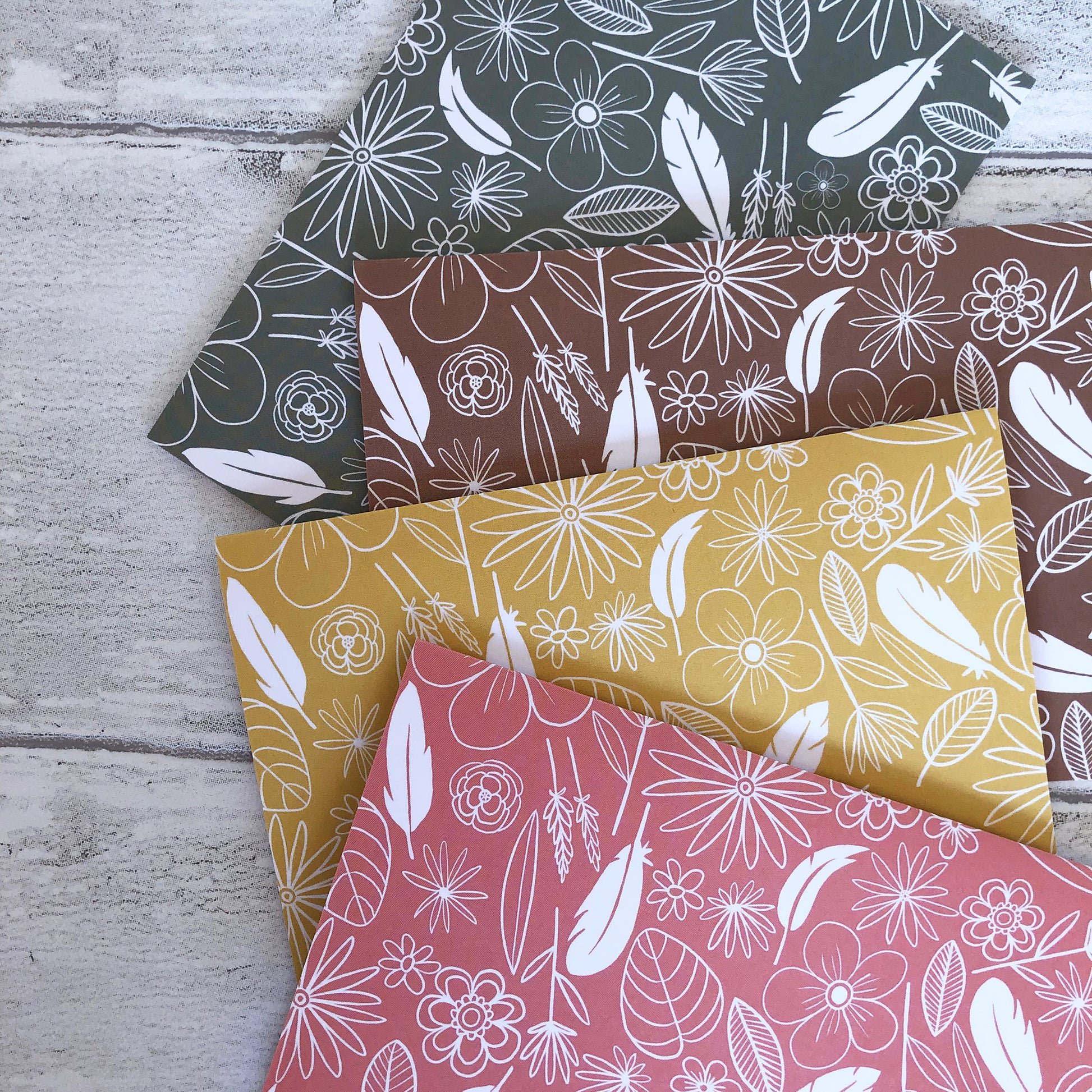 Image shows a collection of 4 notecards in pastel colours with white illustrations of flowers, feathers and leaves.