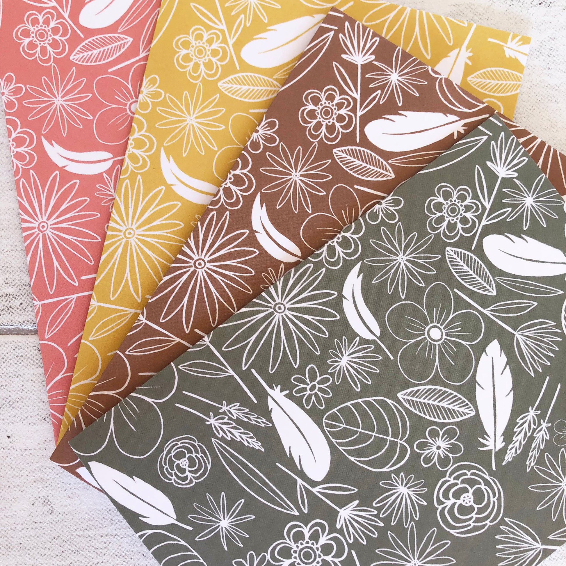 Image shows a collection of 4 notecards in pastel colours with white illustrations of flowers, feathers and leaves.