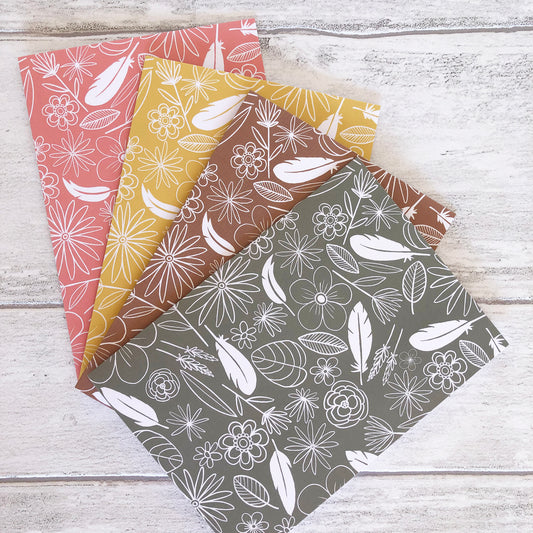 Image shows a collection of 4 notecards in pastel colours with white illustrations of flowers, feathers and leaves.
