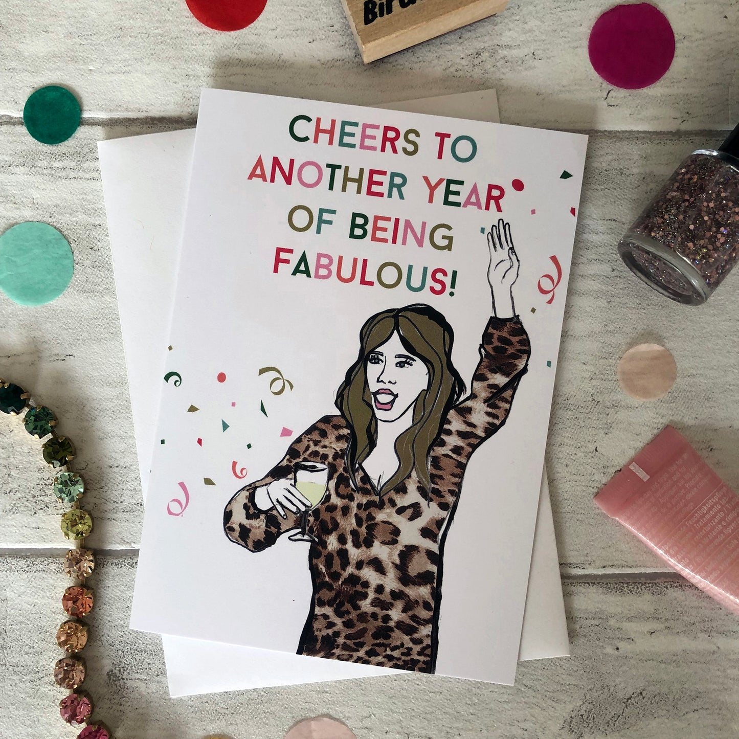 Image shows a fun and fabulous white birthday card with an illustration of a woman in a leopard print top holding a glass of wine and the wording 'Cheers to another year of being fabulous..