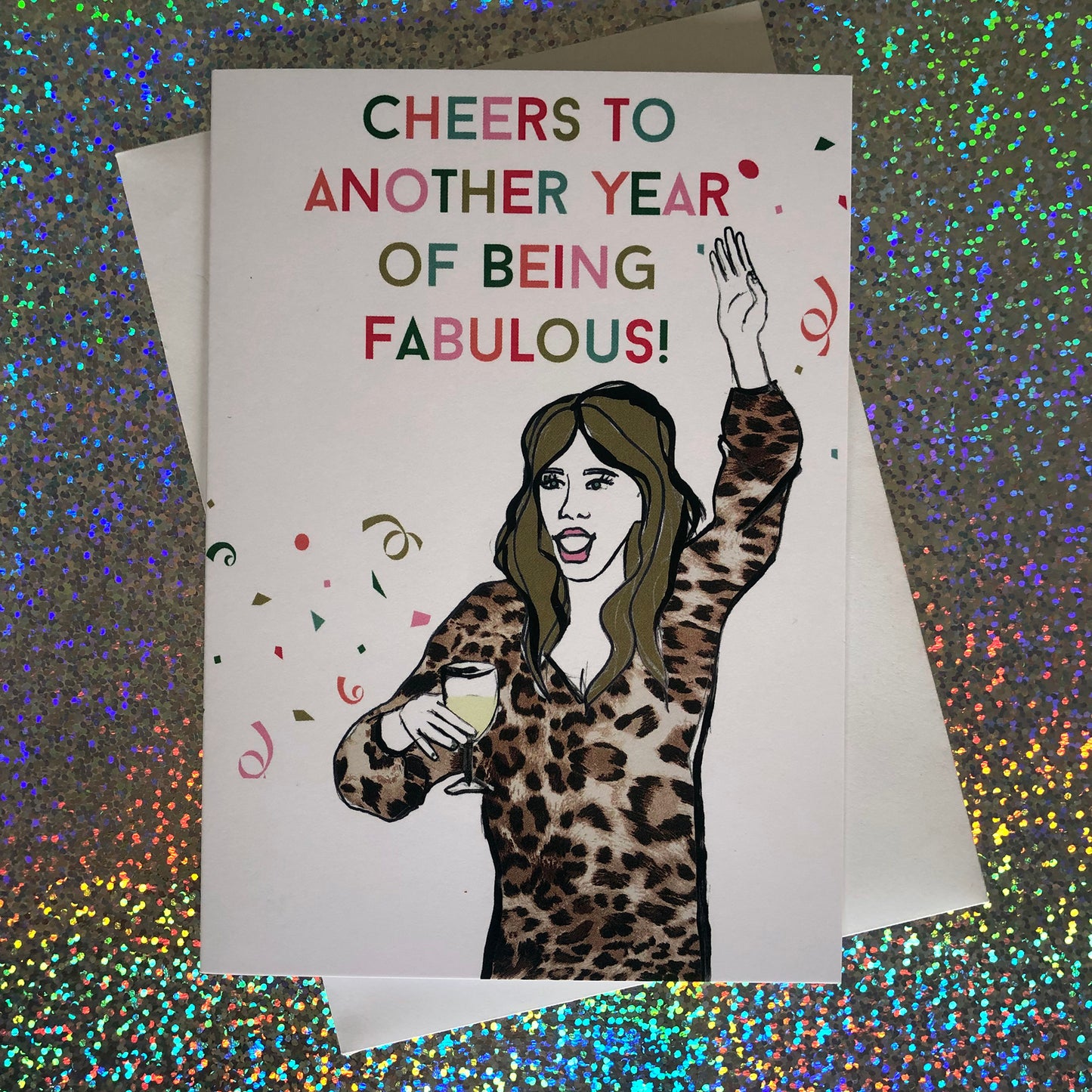 Image shows a fun and fabulous white birthday card with an illustration of a woman in a leopard print top holding a glass of wine and the wording 'Cheers to another year of being fabulous..