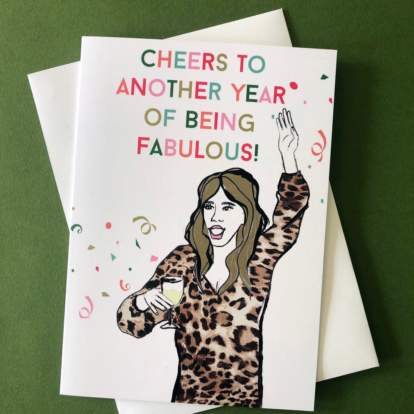 Image shows a fun and fabulous white birthday card with an illustration of a woman in a leopard print top holding a glass of wine and the wording 'Cheers to another year of being fabulous..