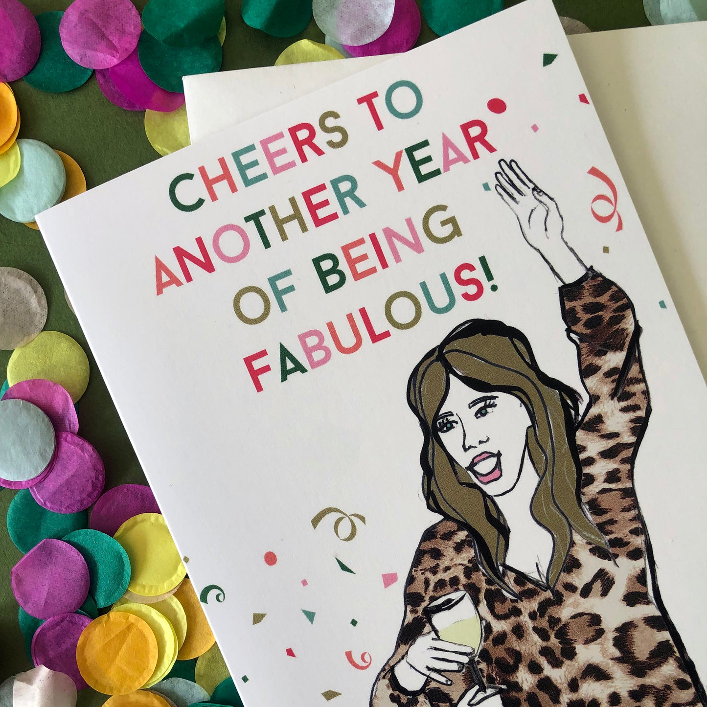Image shows a fun and fabulous white birthday card with an illustration of a woman in a leopard print top holding a glass of wine and the wording 'Cheers to another year of being fabulous..