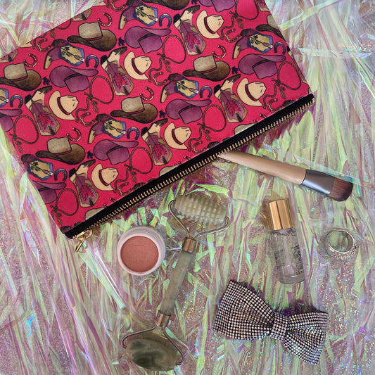 Image shows a bright cherry pink zip pouch with a fun western themed design, featuring cowgirl accessories, hats and boots.
