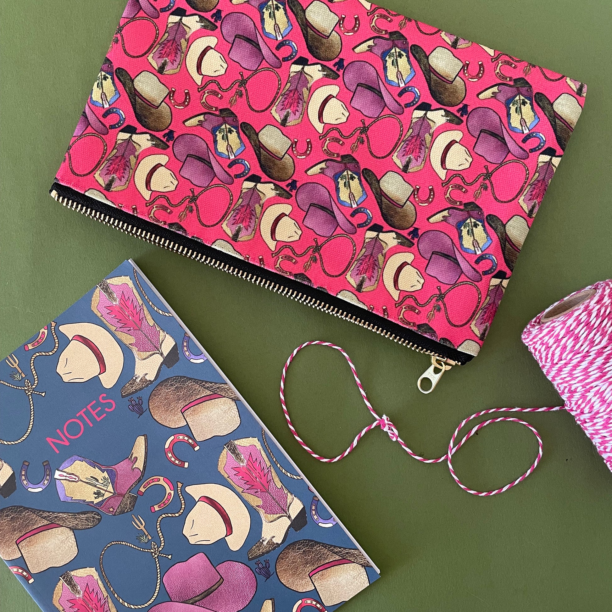 Image shows a bright cherry pink zip pouch with a fun western themed design, featuring cowgirl accessories, hats and boots.