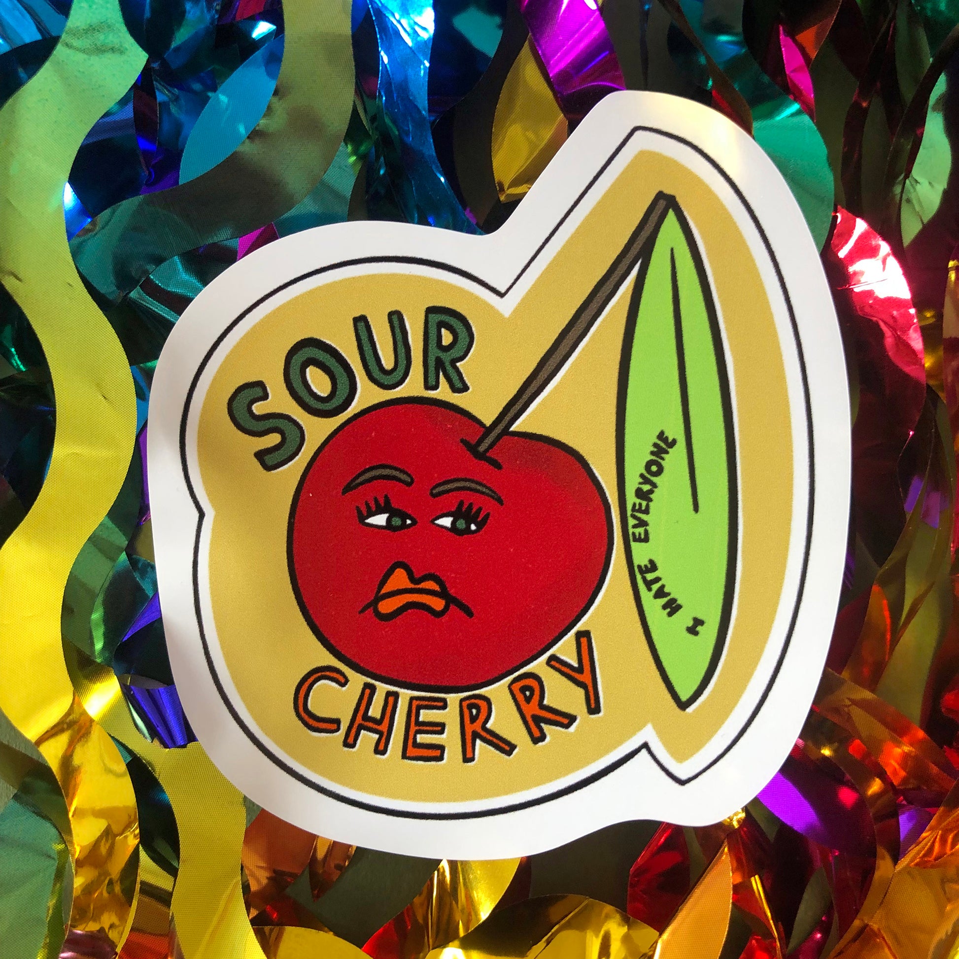 Image shows a vinyl sticker featuring an illustration of an unhappy looking cherry and the wording 'Sour Cherry'