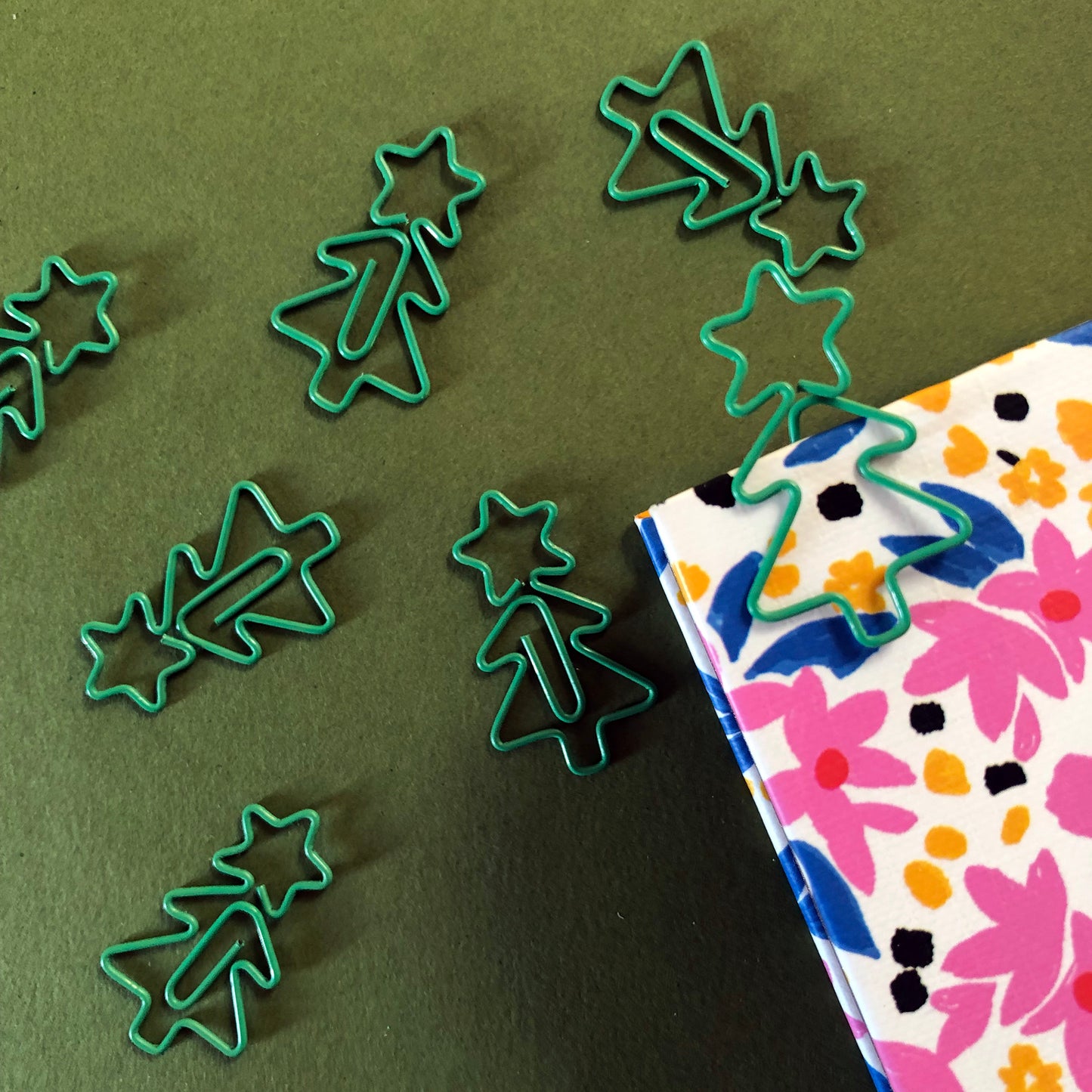 Image shows a collection of cute Christmas tree shaped paperclips on a green background.