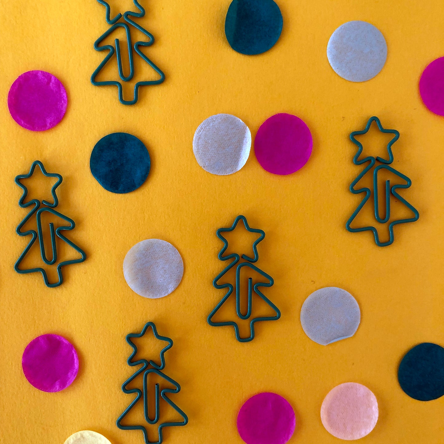 Image shows a collection of cute Christmas tree shaped paperclips on a yellow background.