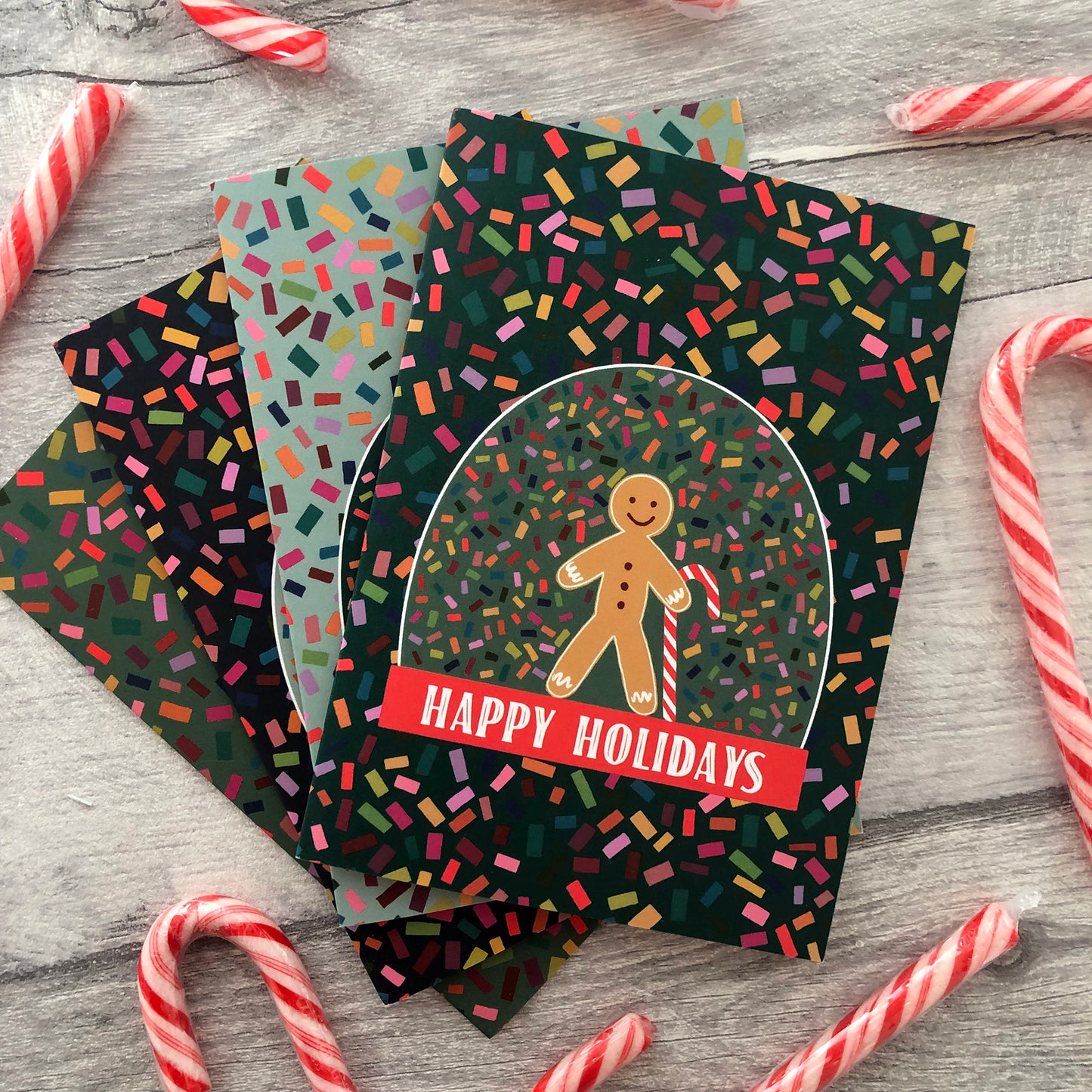 Image shows a collection of bright and colourful Christmas cards featuring illustrations of a snow globe on a confetti patterned background.