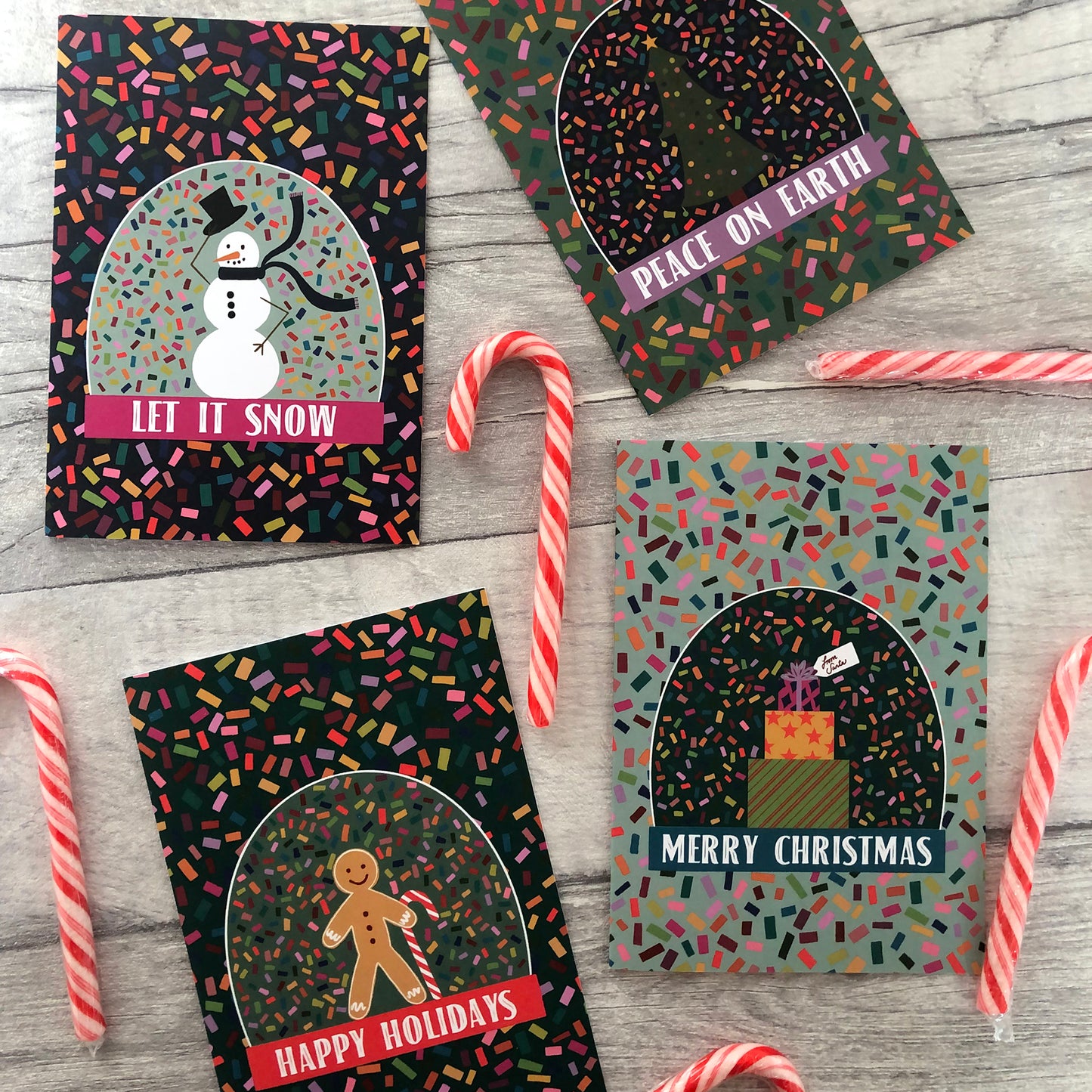 Image shows a collection of bright and colourful Christmas cards featuring illustrations of a snow globe on a confetti patterned background.