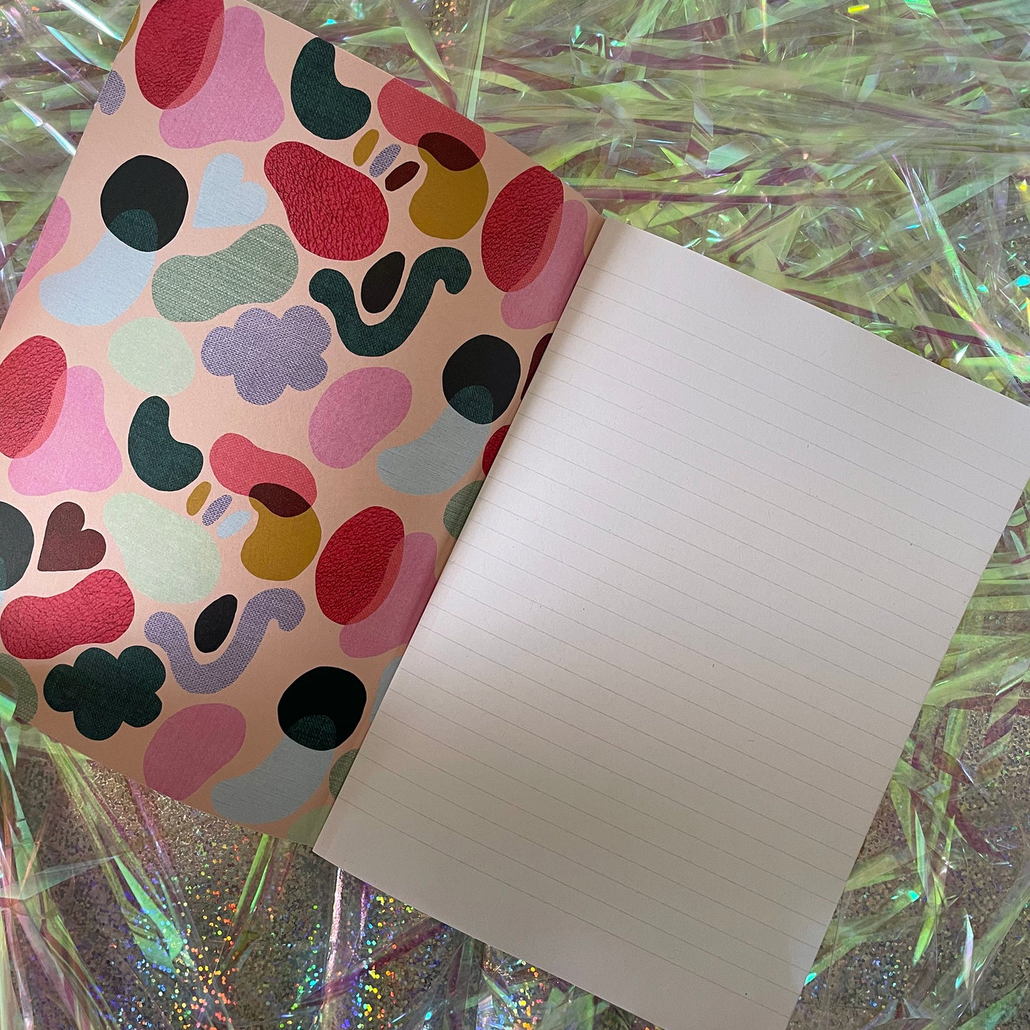 Image of an open notebook with lined pages and a colourful inside cover with a textured shapes pattern in bright colours