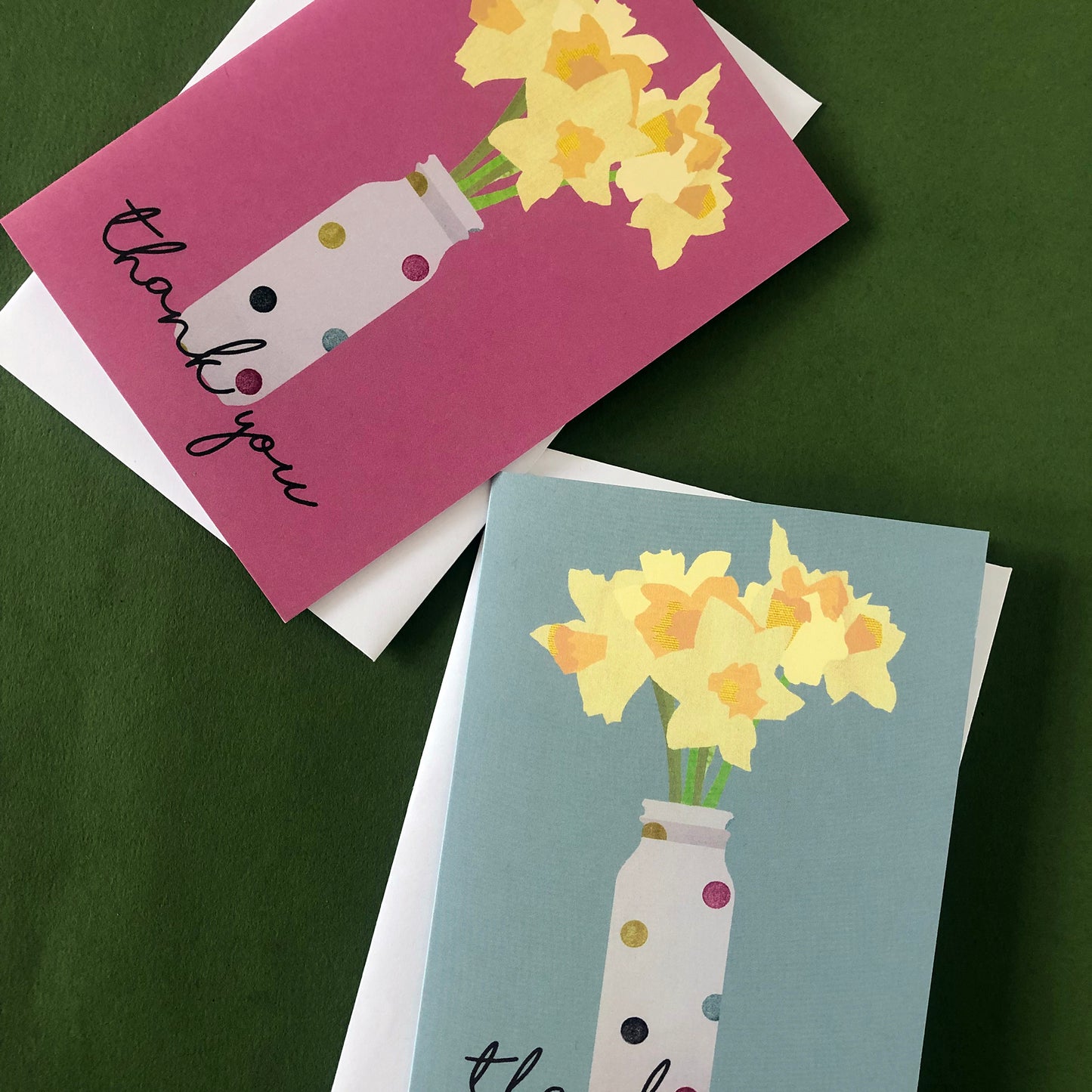 Images shows two greetings cards, one pink and one duck egg blue, both with daffodils in spotty vases and the words 'thank you'