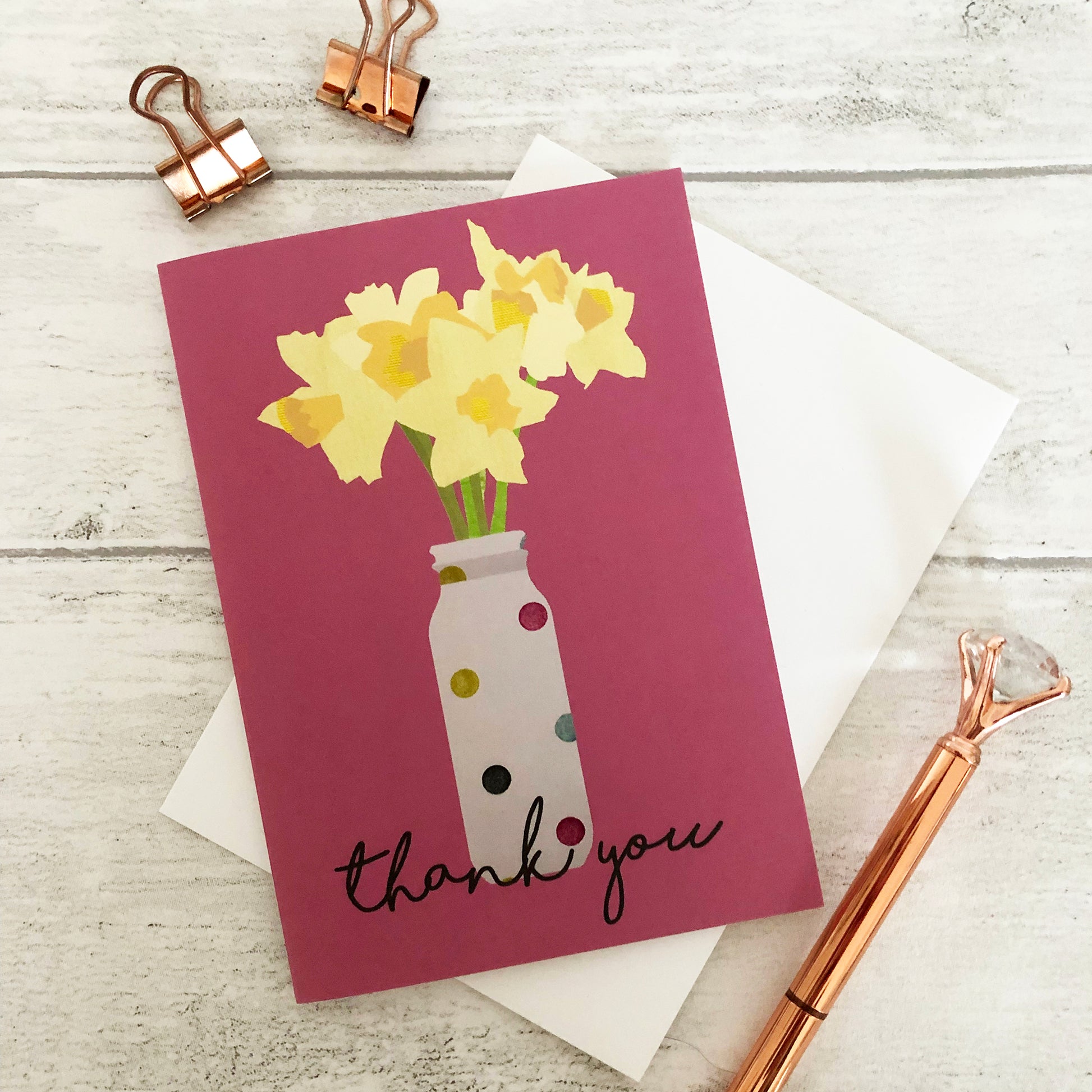 Images shows a pink greetings card with an illustration of daffodils in a spotty vase and the words 'thank you'
