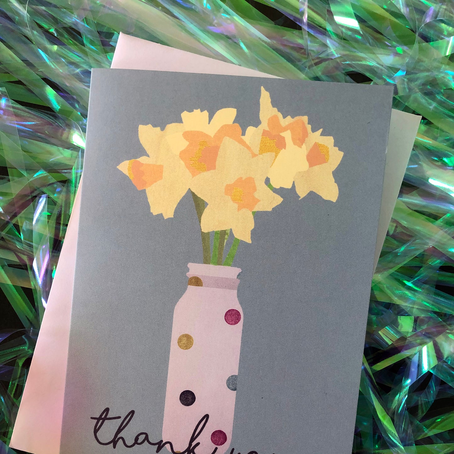 Images shows a blue greetings card with an illustration of daffodils in a spotty vase and the words 'thank you'