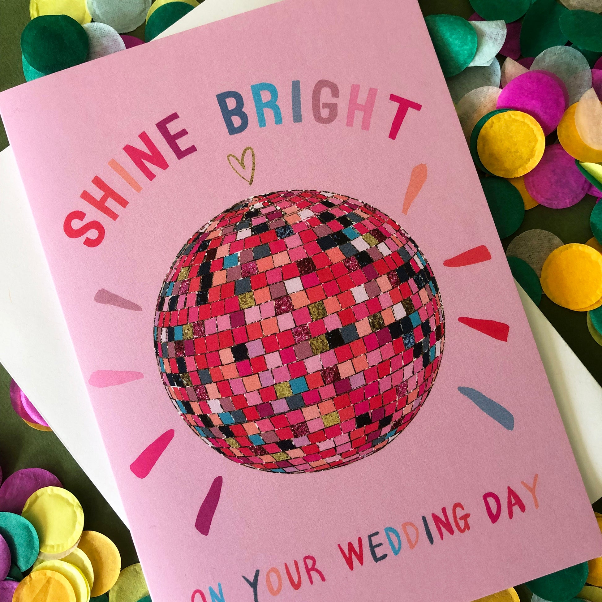 Image shows a pink wedding card featuring a glittery rainbow disco ball illustration and the words 'Shine Bright on your wedding day'.