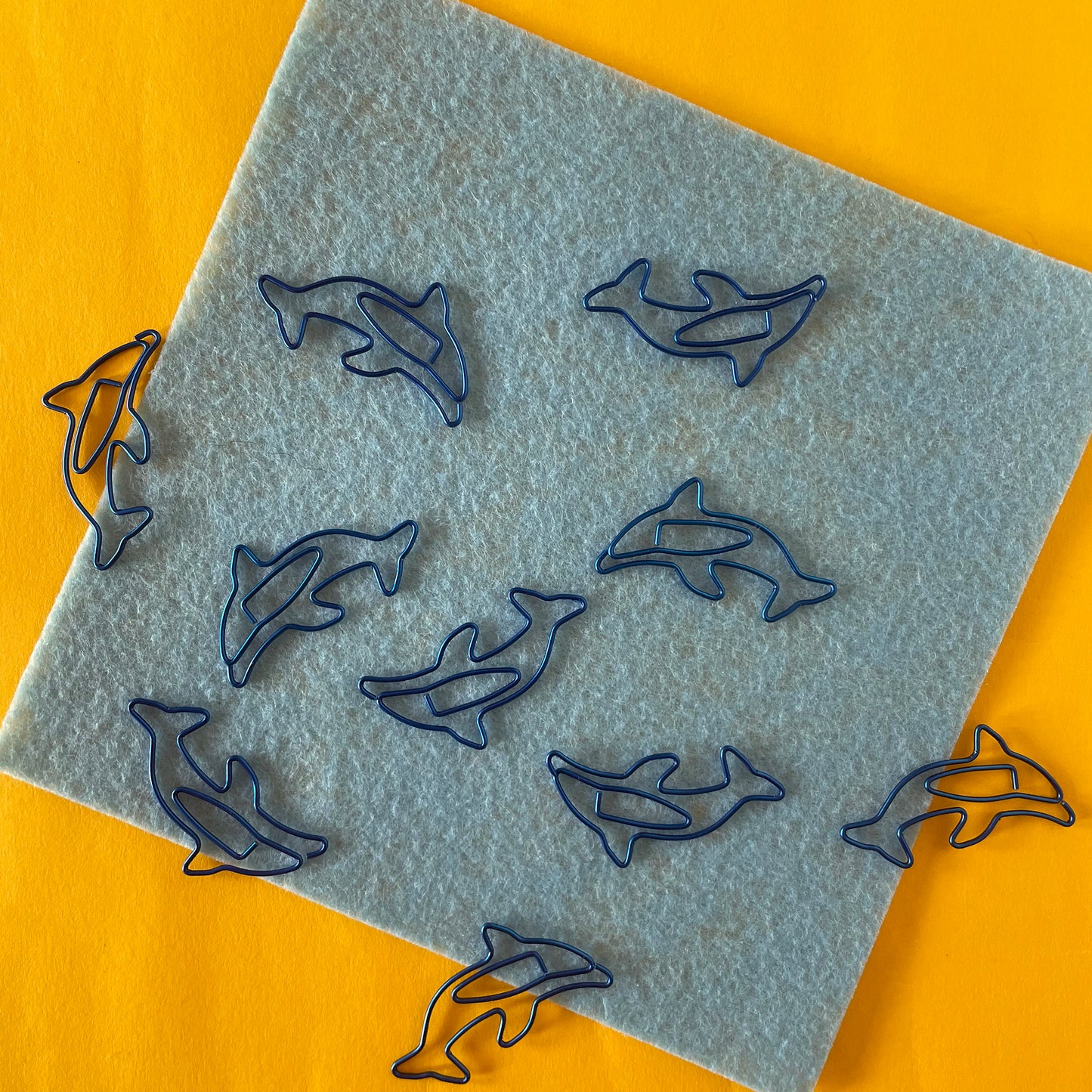 Image shows a fun set of 10 dolphin shaped paper clips in bright, metallic blue