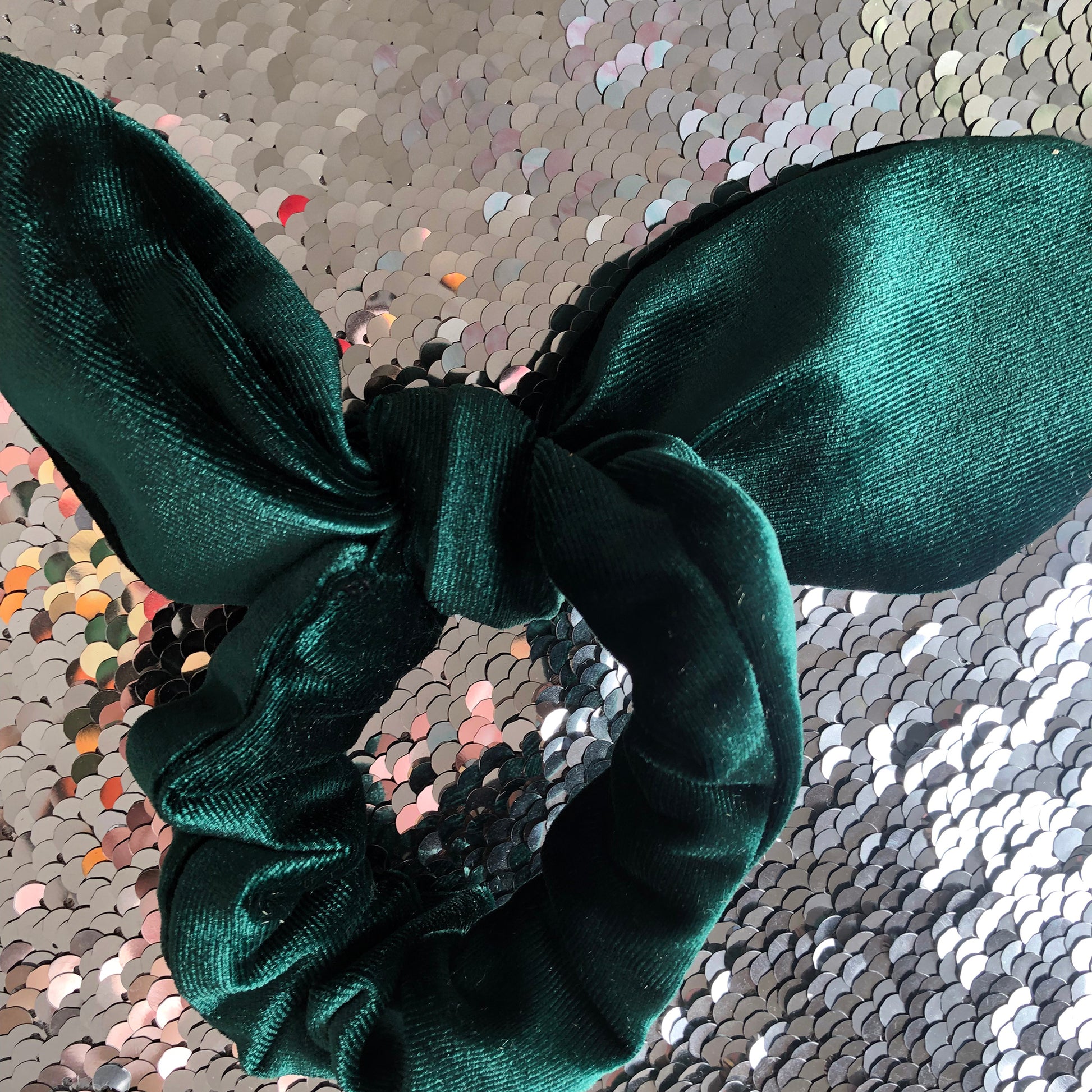 Image shows an emerald green velvet hair scrunchie with a knot and bow