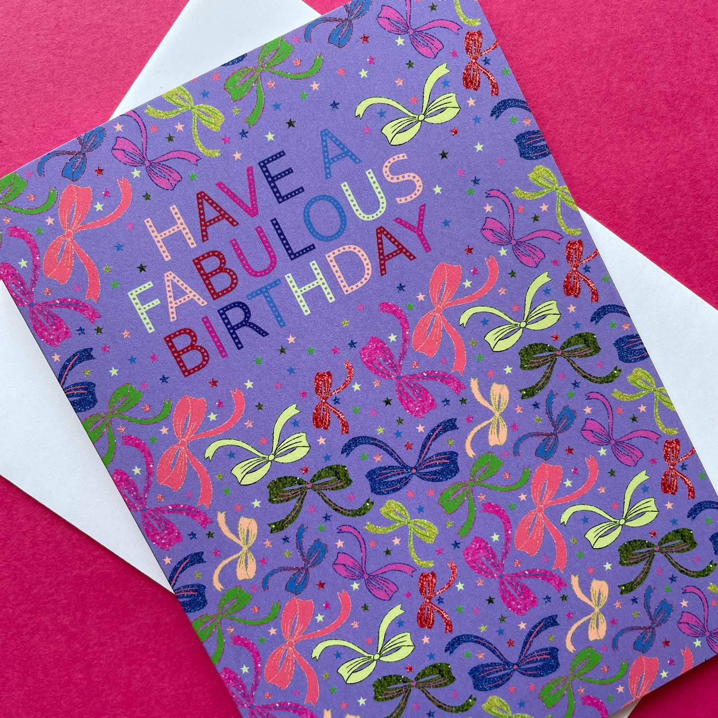 Image shows a lilac birthday card with neon and sparkly bow illustrations and a cloud with multicoloured wording that reads 'Have a fabulous birthday"