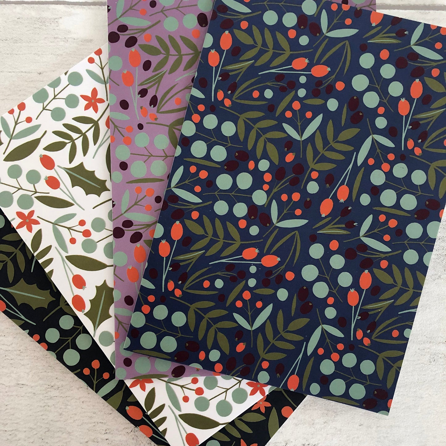 Image shows a collection of festive nature christmas cards featuring a leaves and berries pattern.