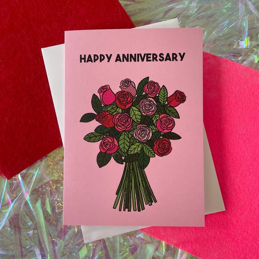 Image shows a light pink greetings card with an illustration of a bunch of roses and the words 'Happy Anniversary'