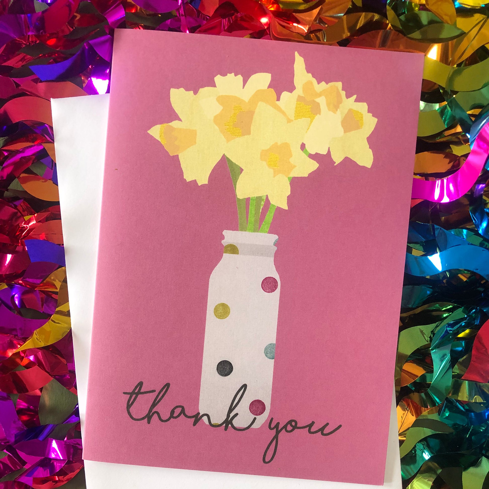 Images shows a pink greetings card with an illustration of daffodils in a spotty vase and the words 'thank you'