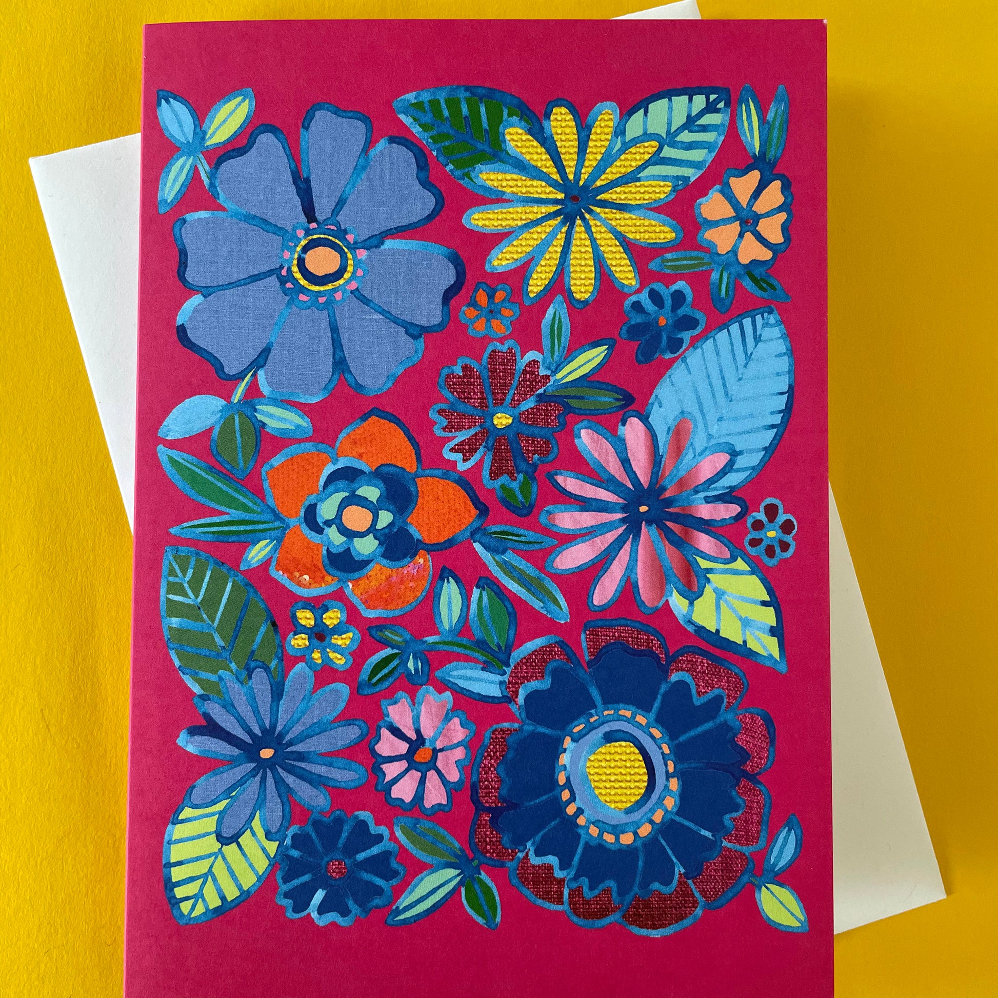 Image shows a bright pink greetings card with a floral illustration in blue ink with colourful collaged detail