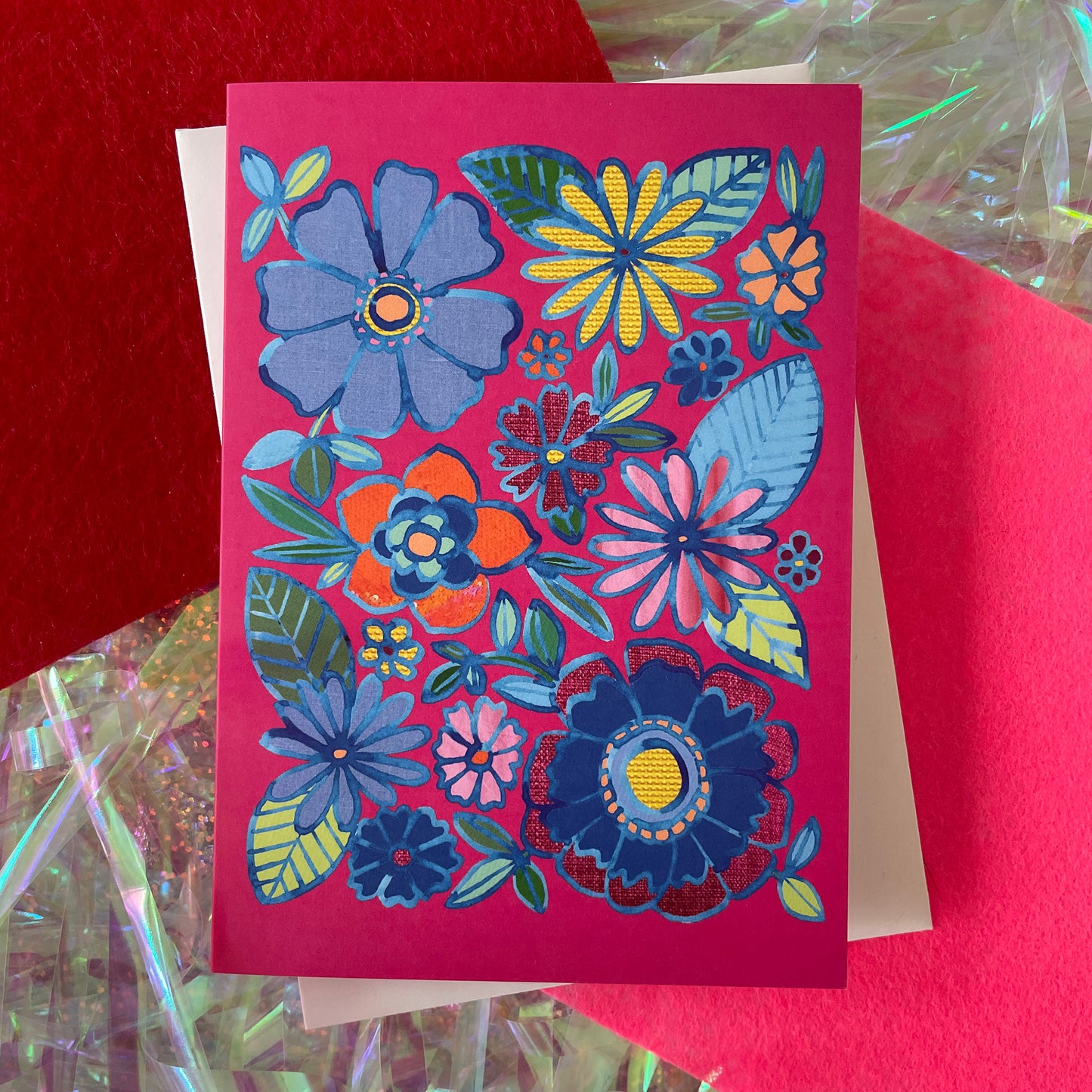Image shows a bright pink greetings card with a floral illustration in blue ink with colourful collaged detail