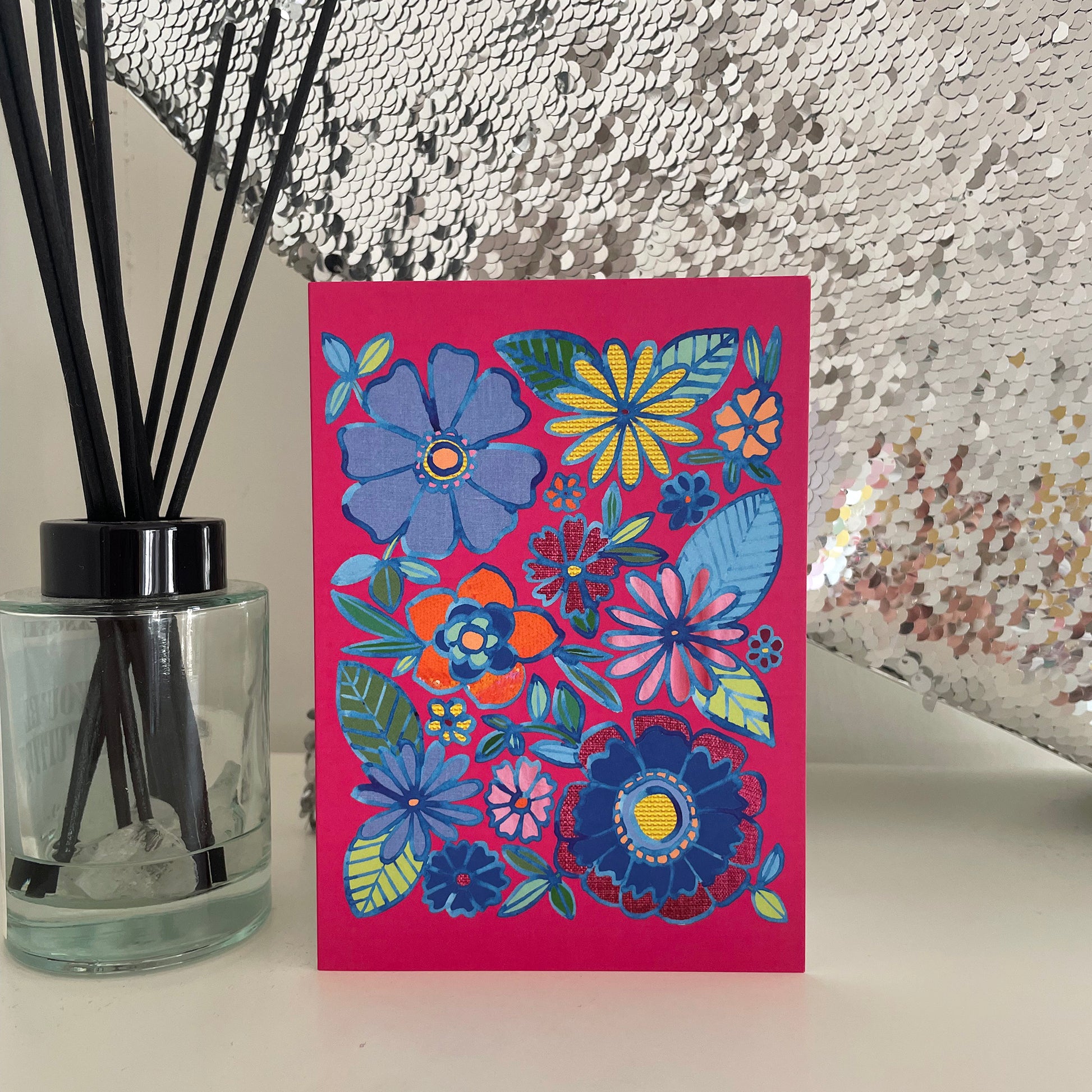 Image shows a bright pink greetings card with a floral illustration in blue ink with colourful collaged detail