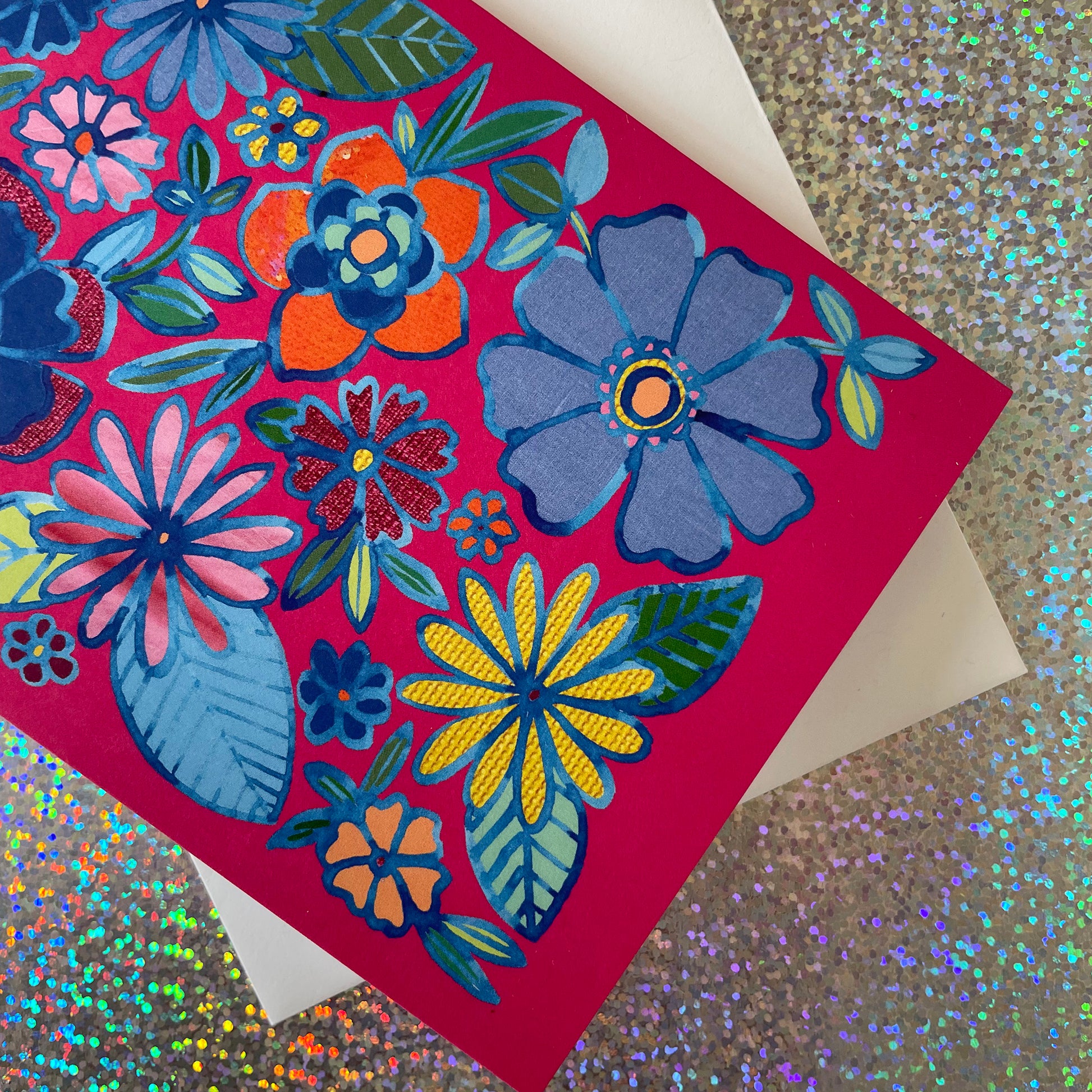 Image shows a bright pink greetings card with a floral illustration in blue ink with colourful collaged detail