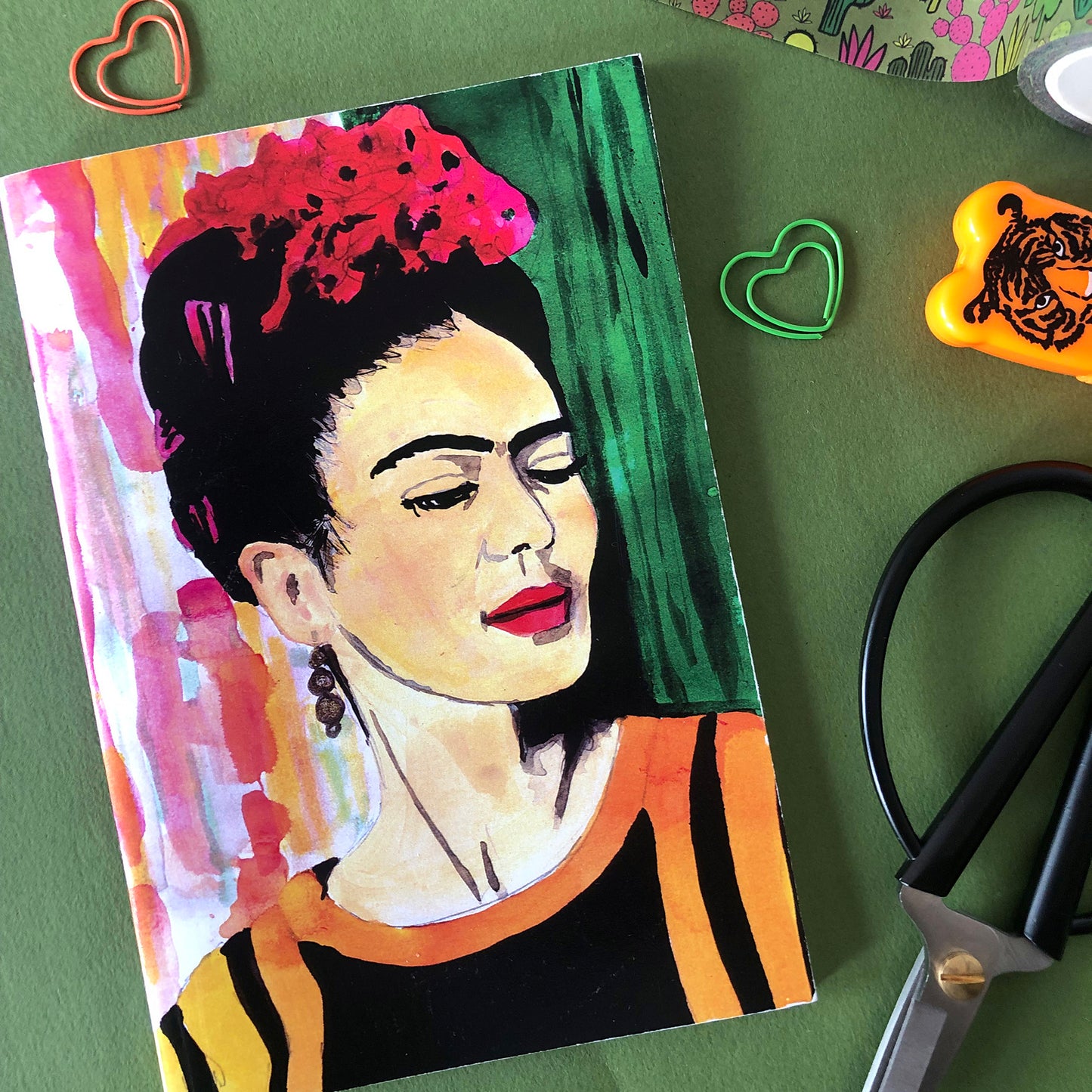 Image shows a full colour notebook featuring a bright, hand painted illustration of Frida Kahlo