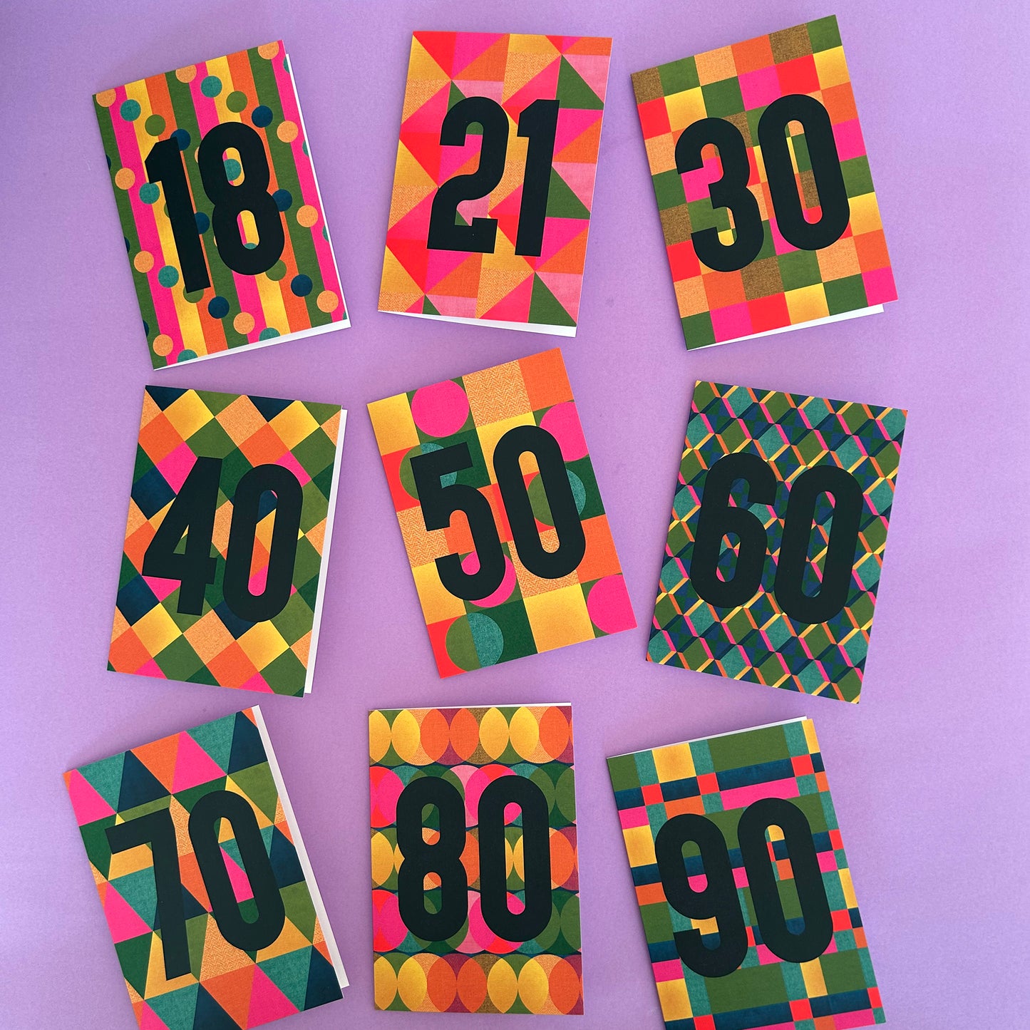 Nine colourful patterned cards arranged in a grid on a lavender background, each printed with a large black number from 18 to 90.