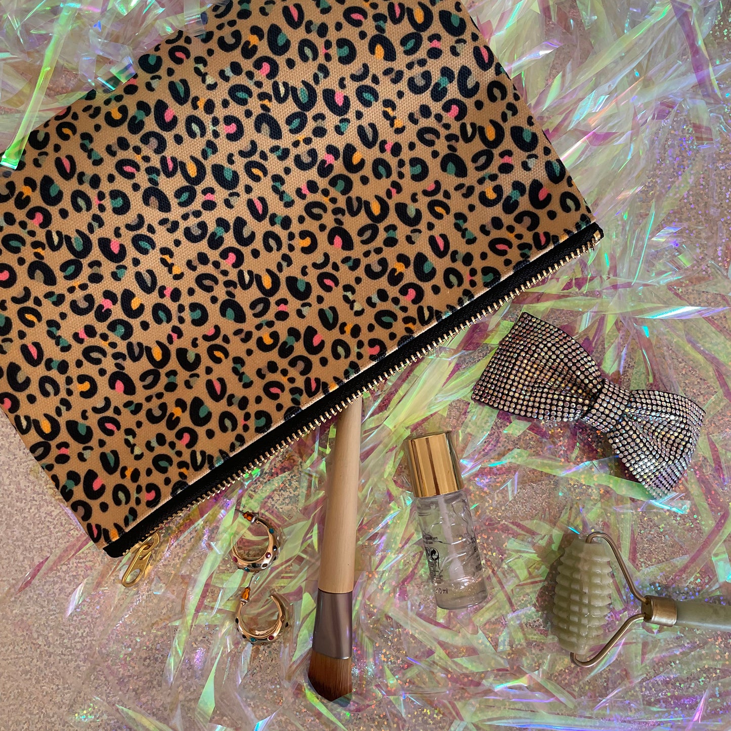 Image shows a beautiful leopard print zip pouch in gold on an iridescent background with accessories.