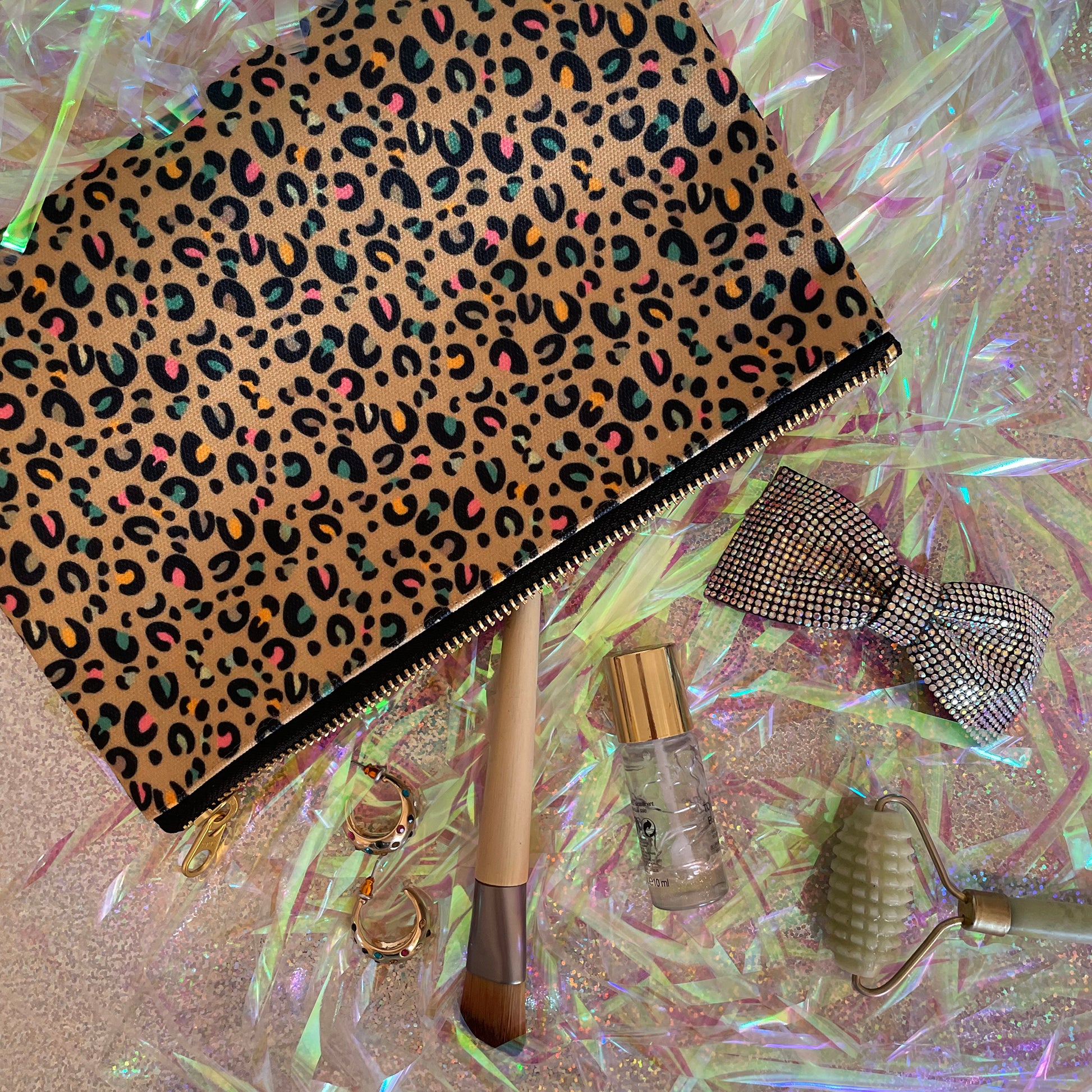Image shows a beautiful leopard print zip pouch in gold on an iridescent background with accessories.