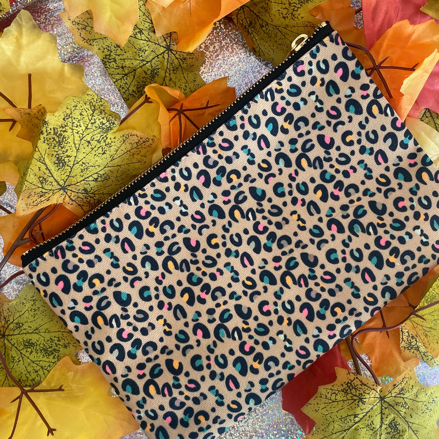 Image shows a beautiful leopard print zip pouch in gold on a background of autumn leaves.