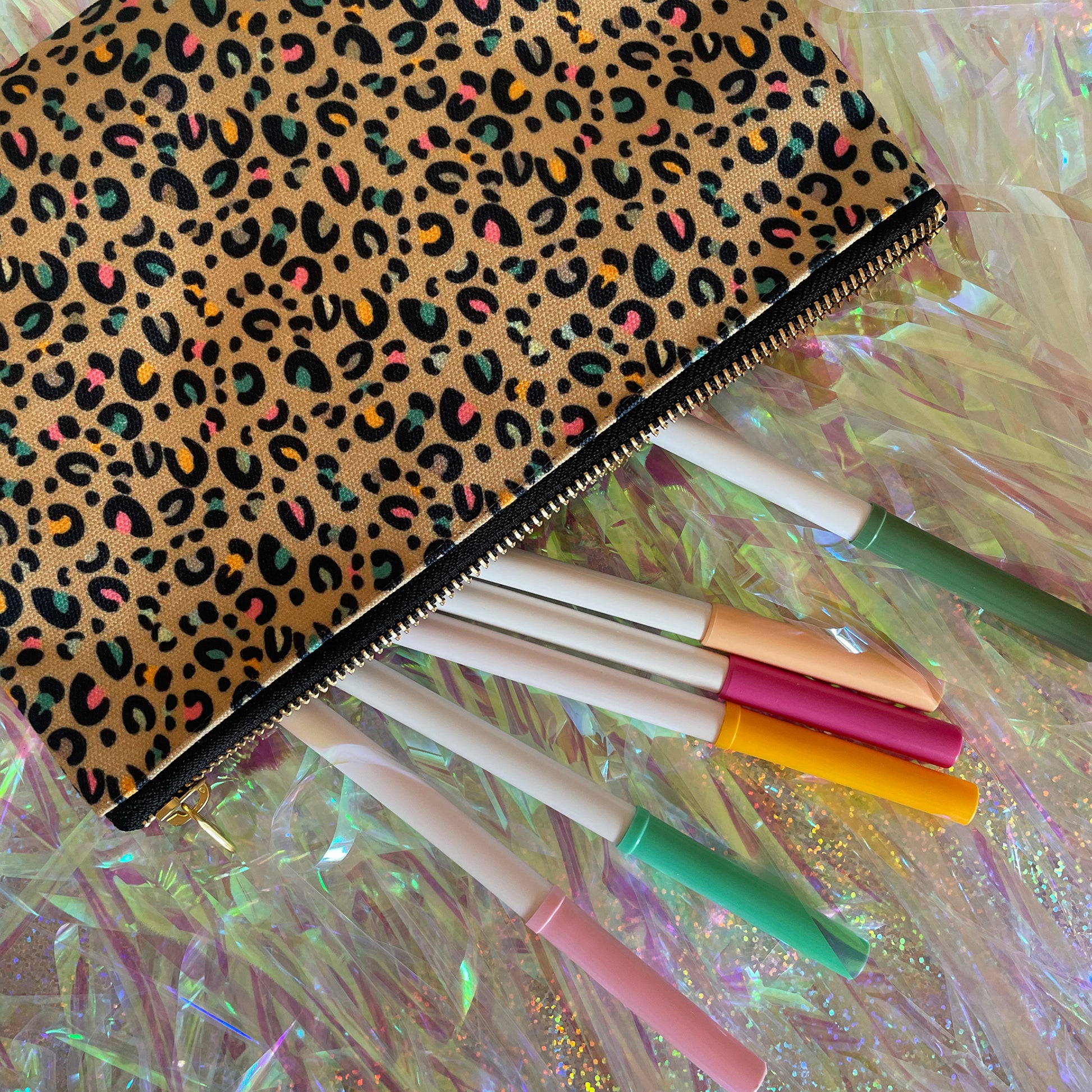Image shows a beautiful leopard print zip pouch in gold on an iridescent background with pens.
