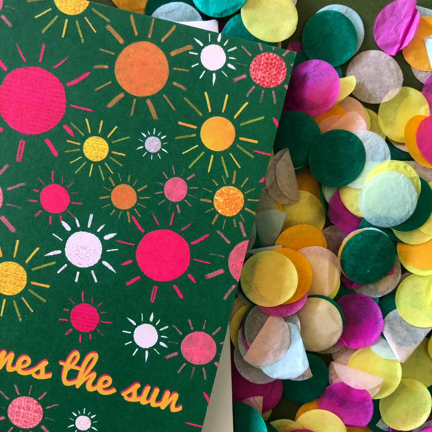 Image shows a green everyday greetings card that says 'here comes the sun' and features a fun pattern of colourful suns
