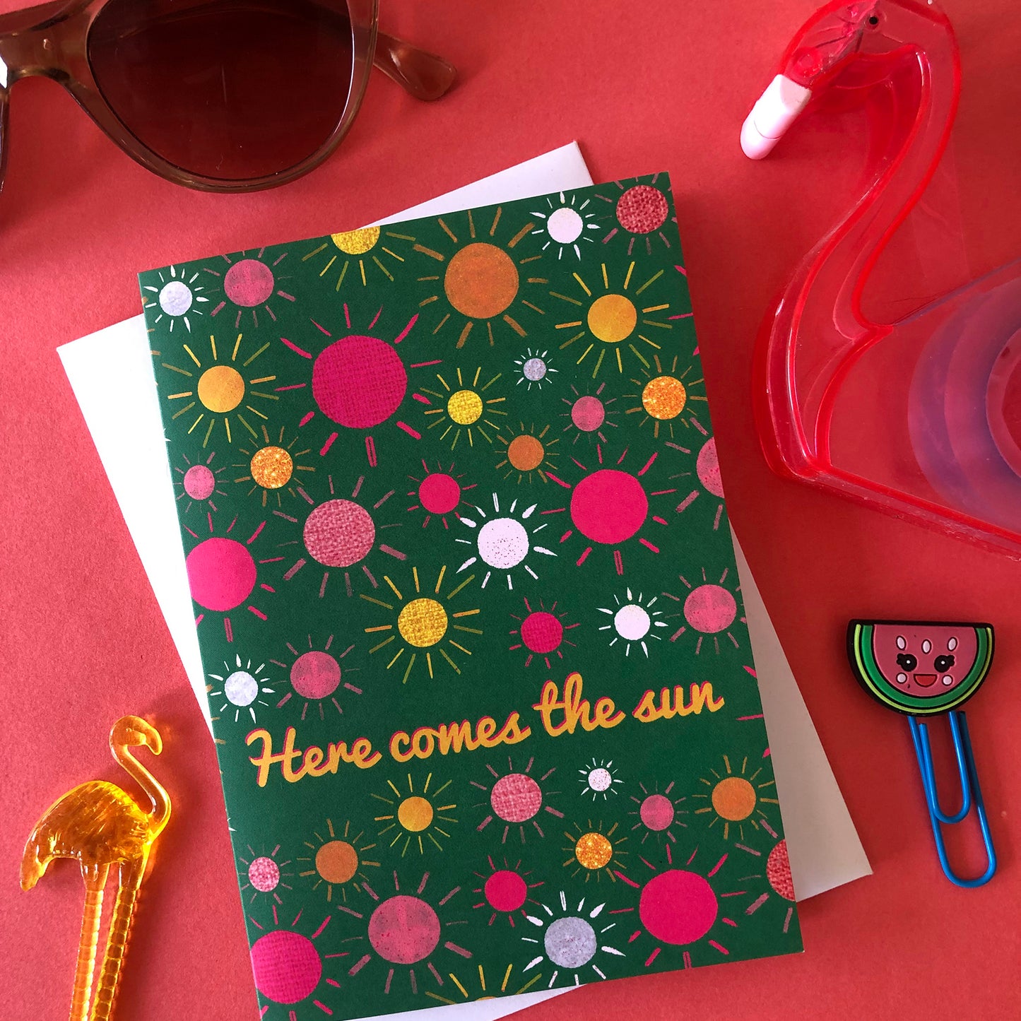 Image shows a green everyday greetings card that says 'here comes the sun' and features a fun pattern of colourful suns
