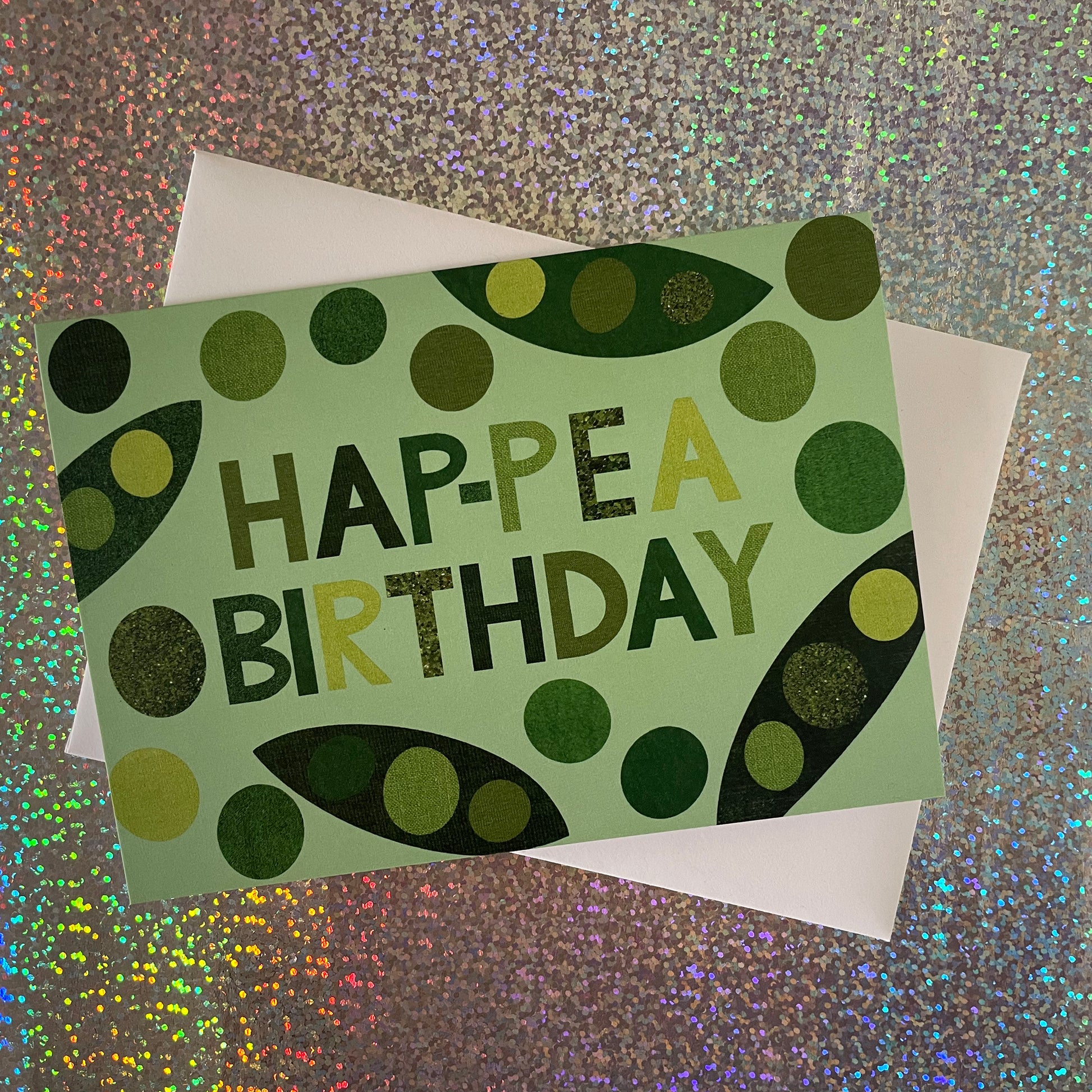 Image of a light green card that says Hap-pea Birthday in bold lettering and has collaged illustrations of peas and pods
