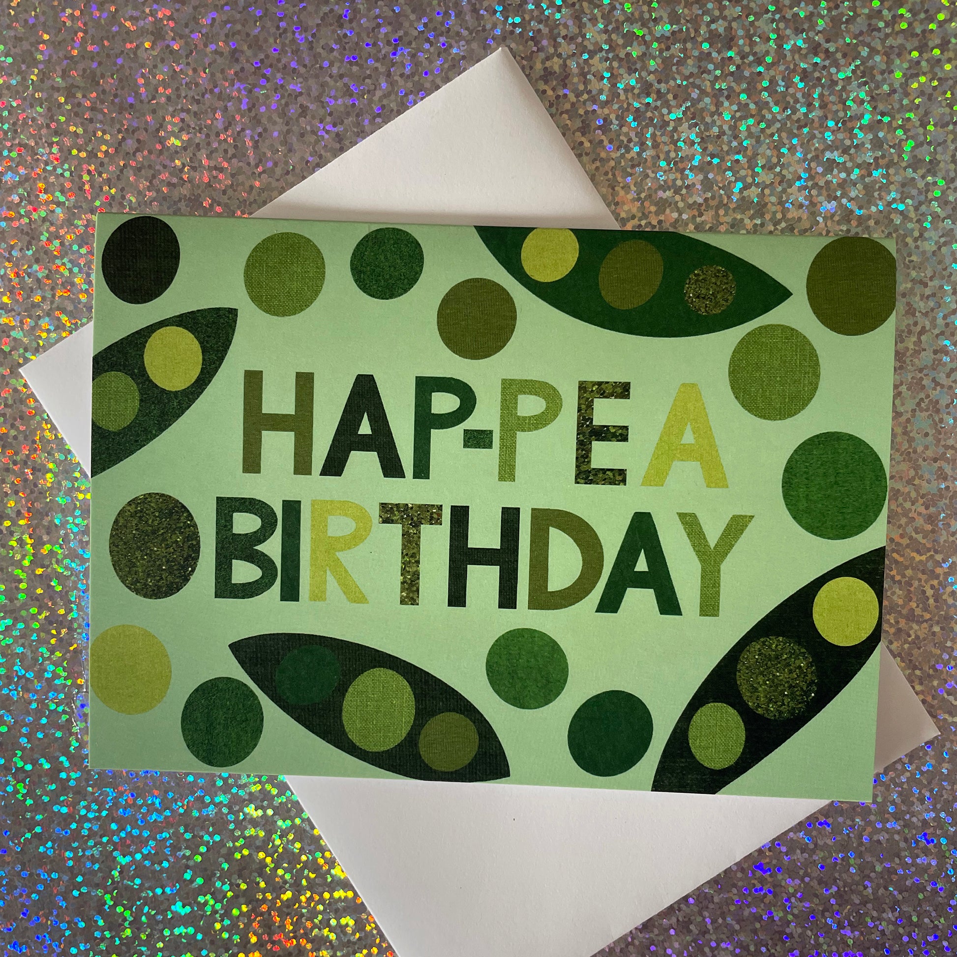 Image of a light green card that says Hap-pea Birthday in bold lettering and has collaged illustrations of peas and pods
