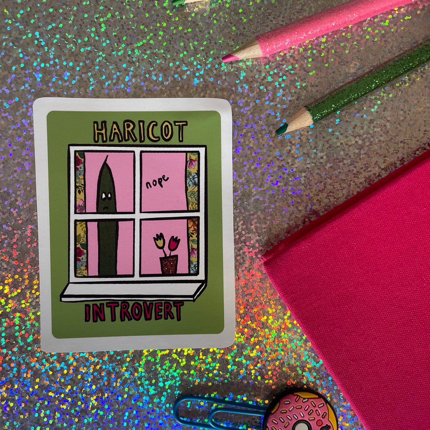 Image shows a green, rectangular sticker with an illustration of a green bean looking out of a window and the words 'Haricot Introvert'