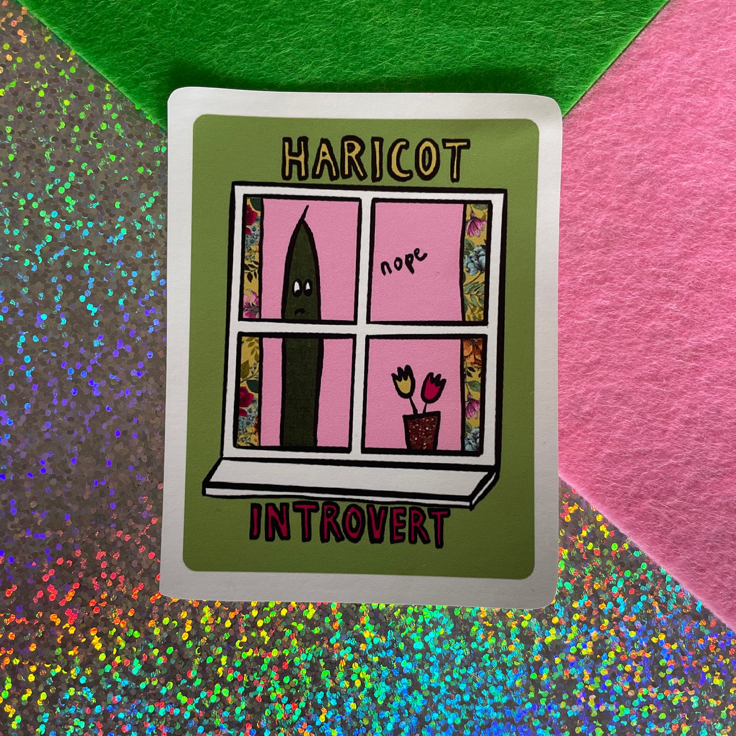 Image shows a green, rectangular sticker with an illustration of a green bean looking out of a window and the words 'Haricot Introvert'