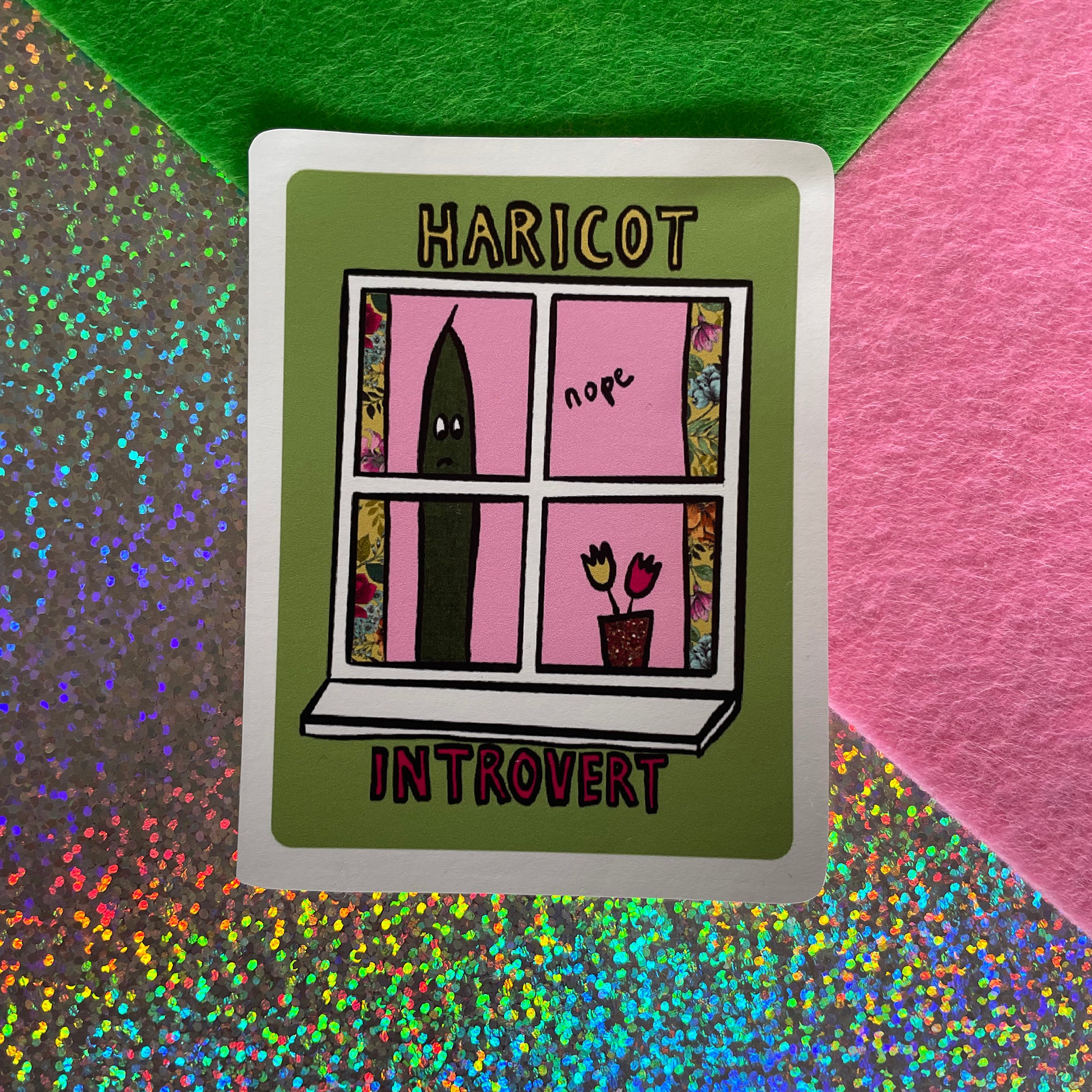 Image shows a green, rectangular sticker with an illustration of a green bean looking out of a window and the words 'Haricot Introvert'